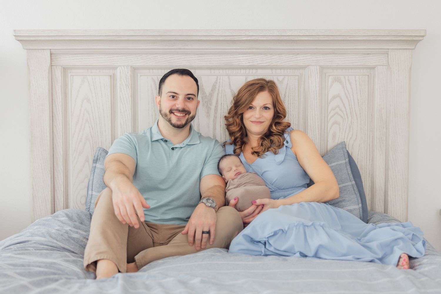 family sitting on bed holding newborn baby smiling for photograph