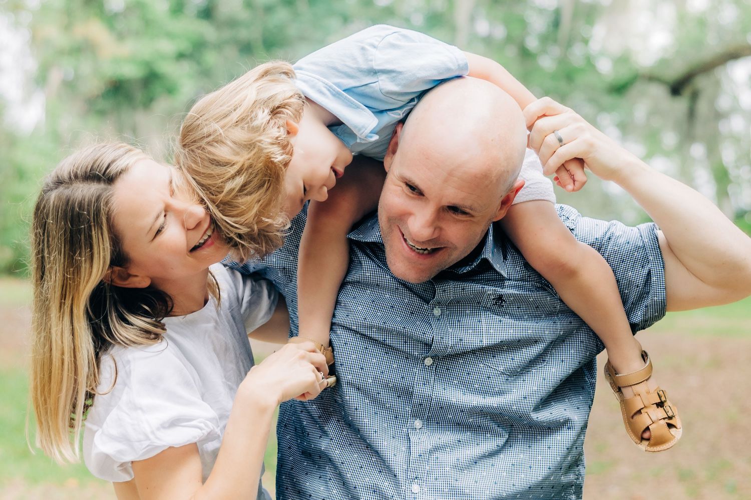 mom laughing as son is on dads shoulders and leaning over to kiss mom