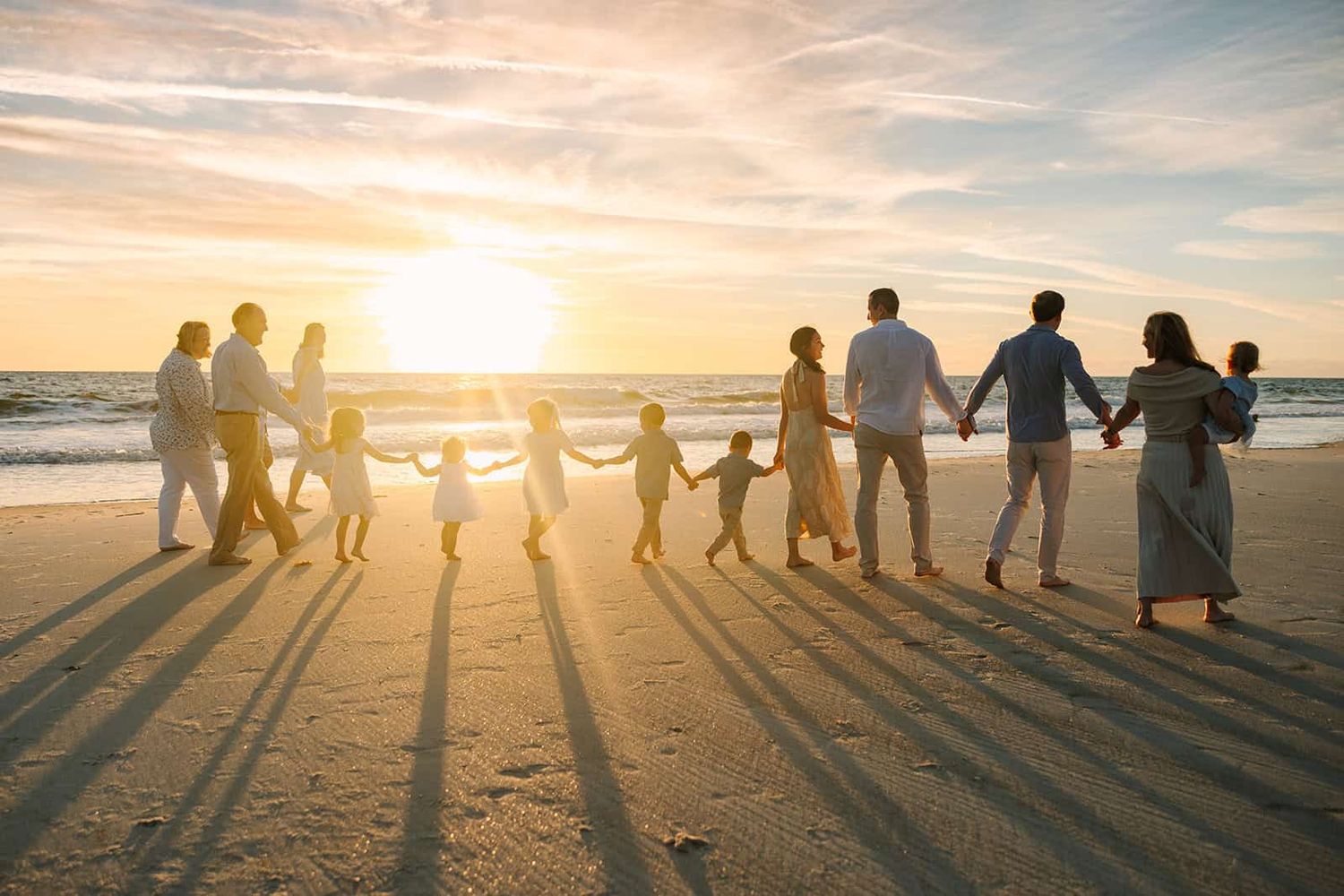large extended family walking down the beach at Jacksonville beach sunrise with sun coming up right over the ocean