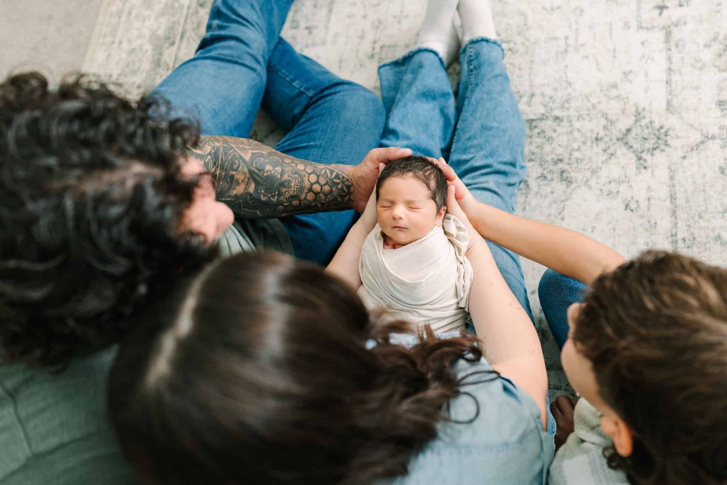 Two parents sitting on floor gazing lovingly at their swaddled newborn baby during an intimate newborn photo session.
