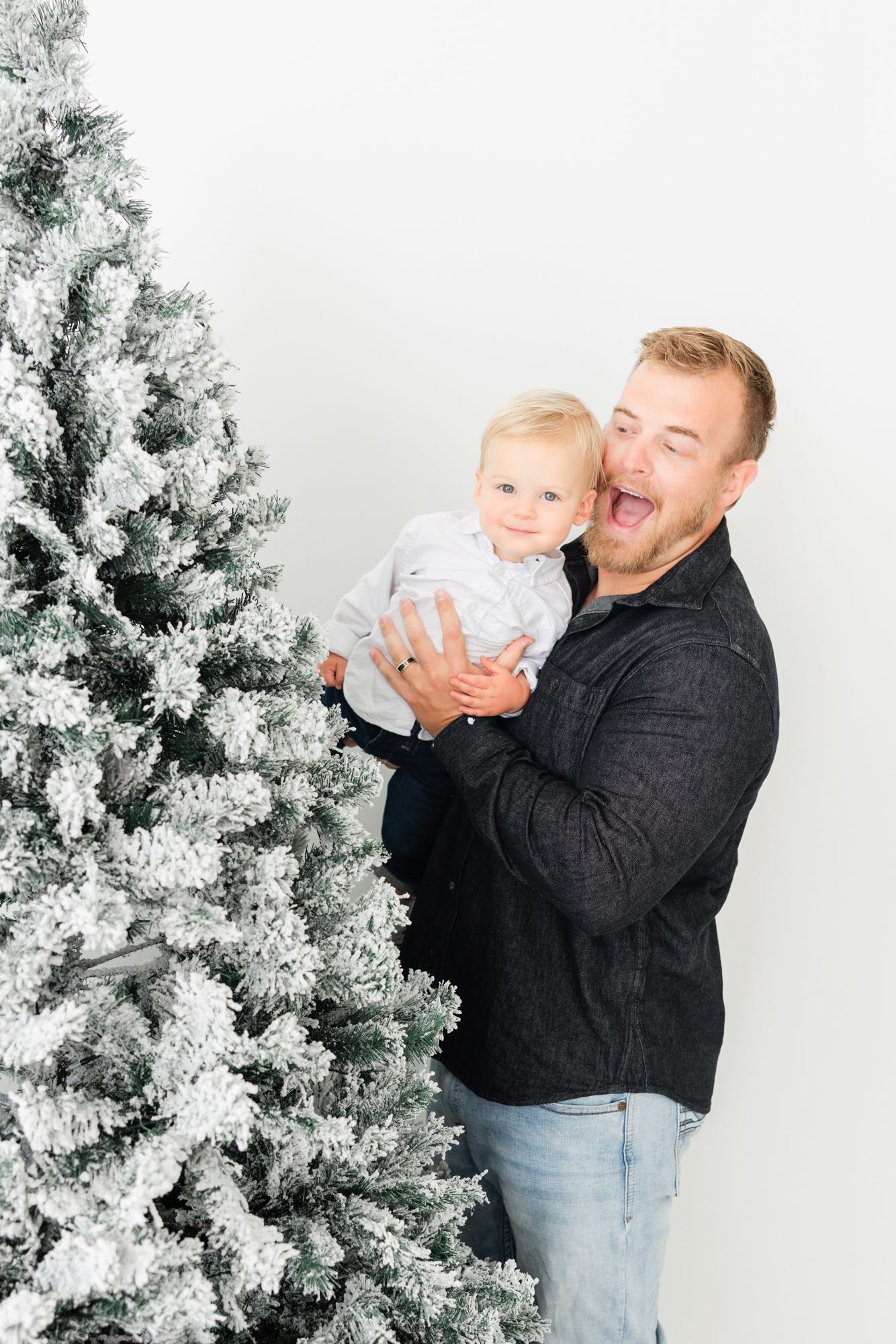 dad and son laughing poking out from behind the Christmas tree