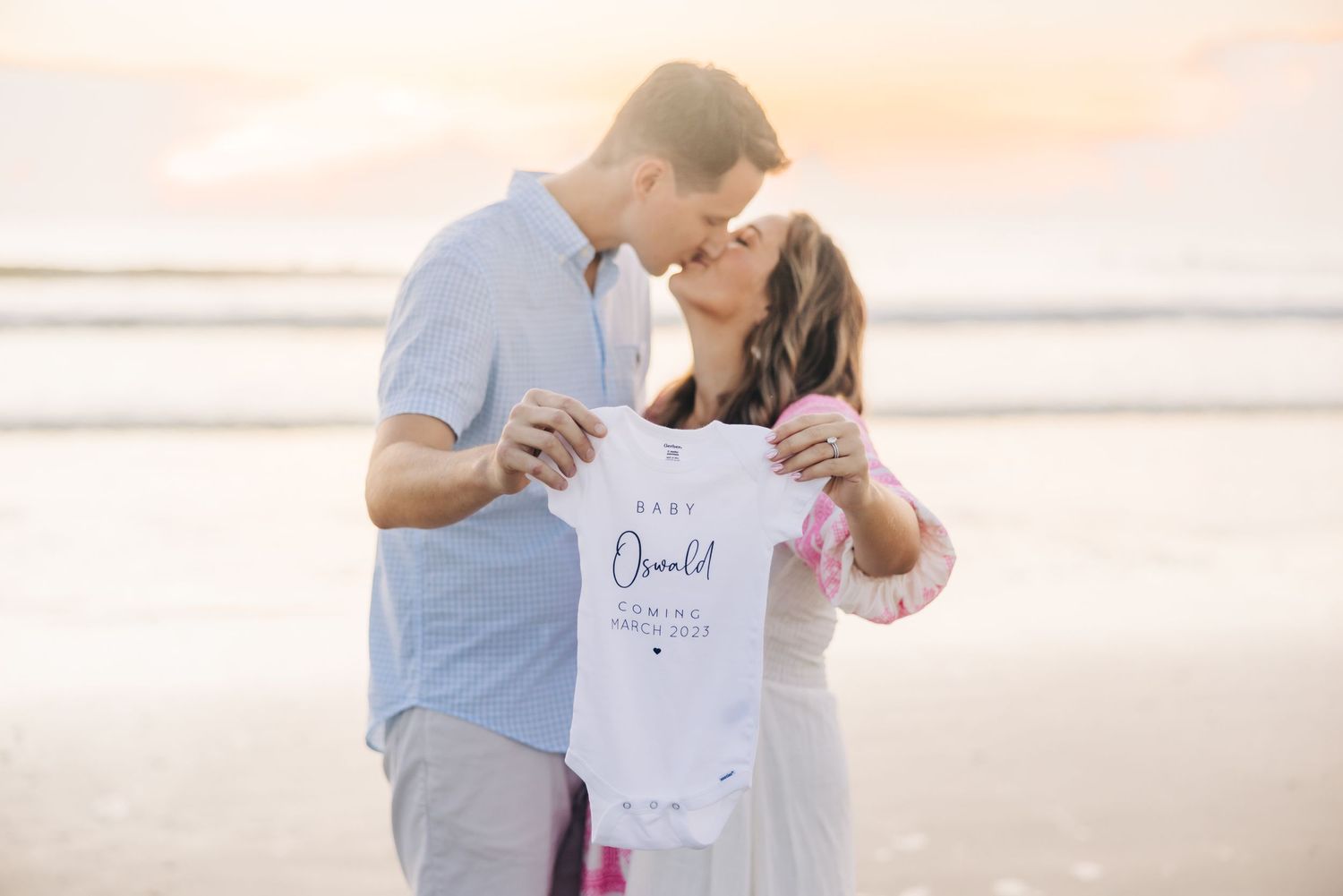pregnancy announcement in jacksonville beach sunrise with parents holding a baby outfit with due date