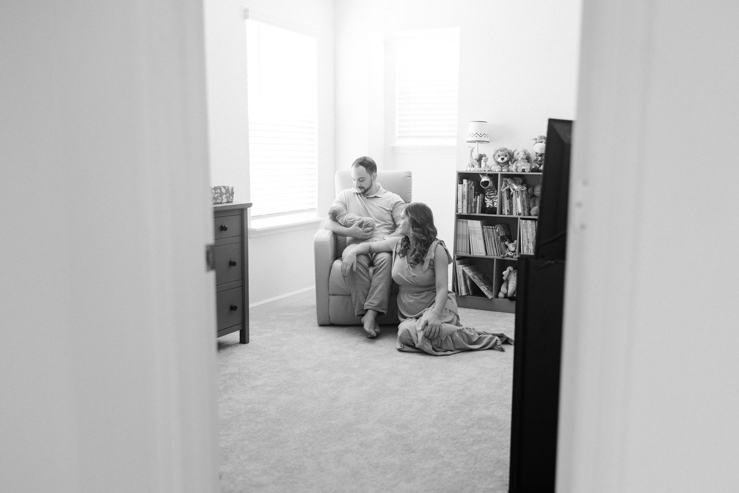 black and white peek into the nursery with parents holding newborn baby