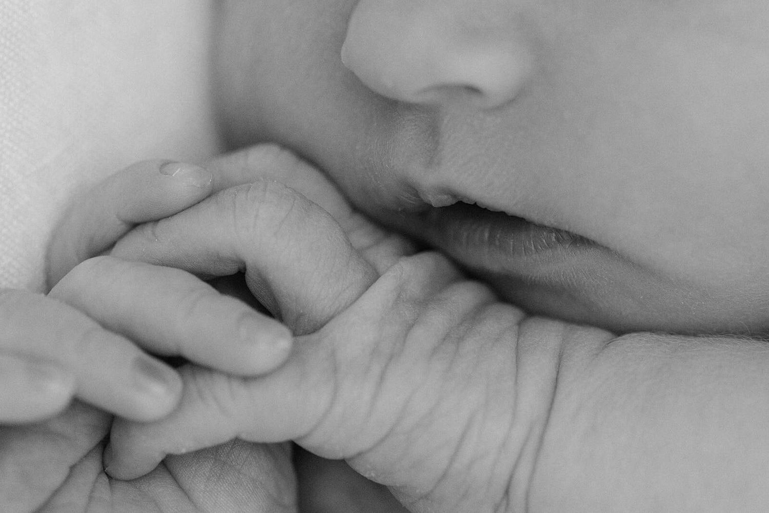 black and white close up of baby hands holding them hear his lips