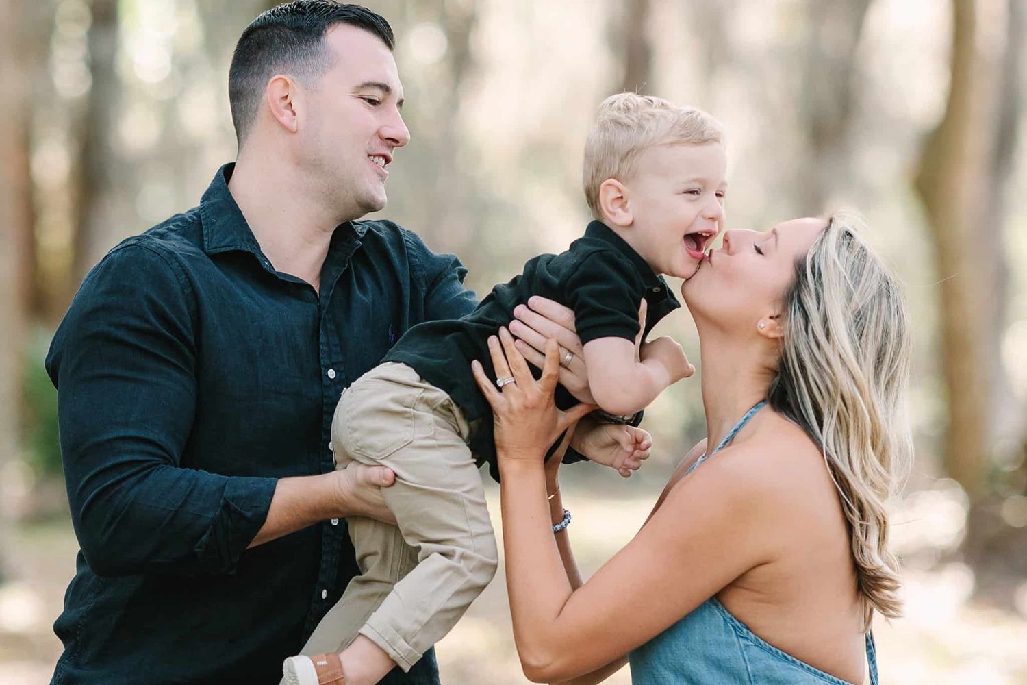 dad lifting toddler boy to give mom kisses and he has a big laugh