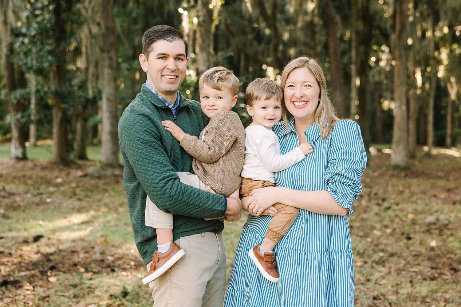 mom and dad each holding one toddle boy on their hip smiling in a park