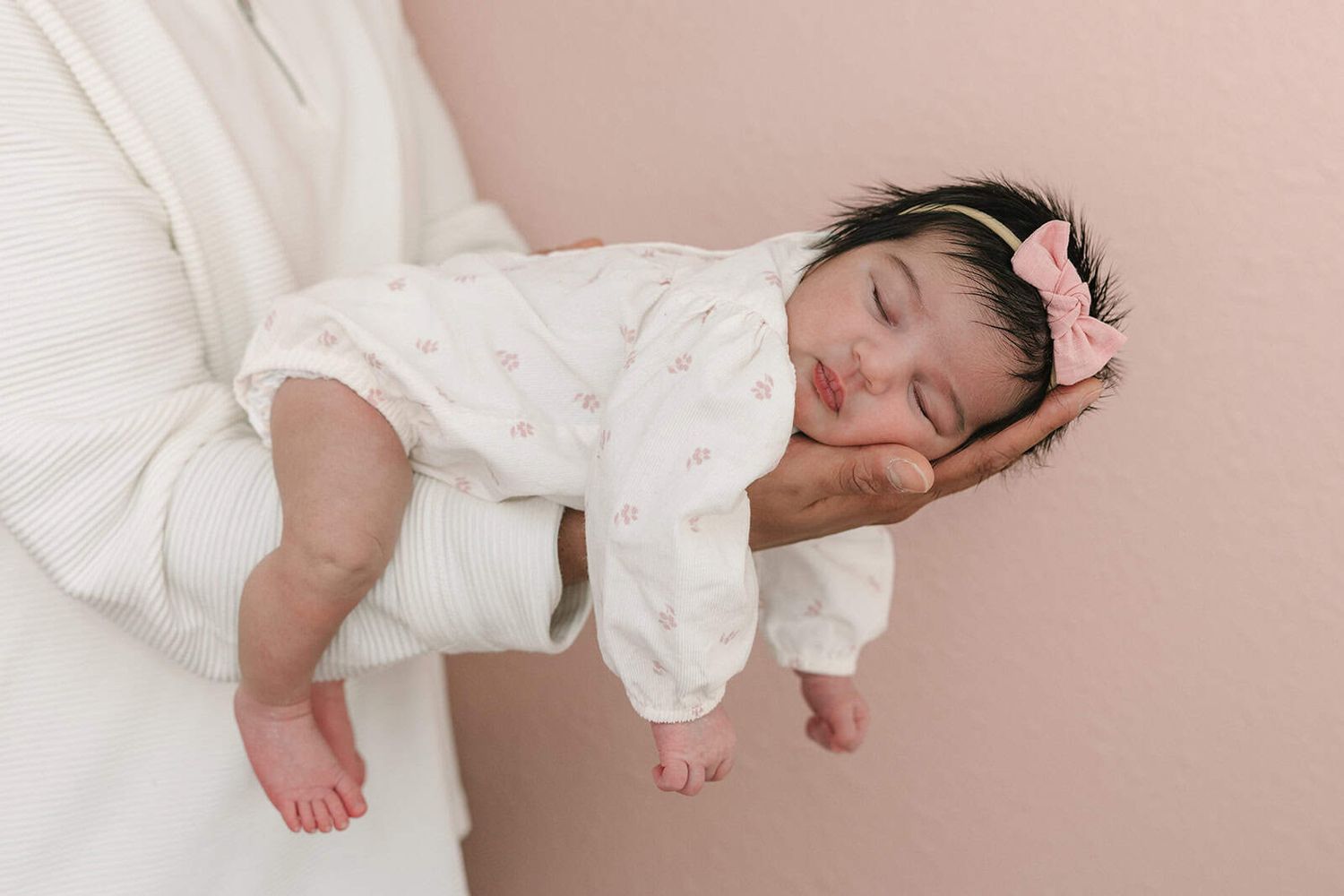 newborn baby girl with a bow on her head laying on dad's arm, showing how little she is
