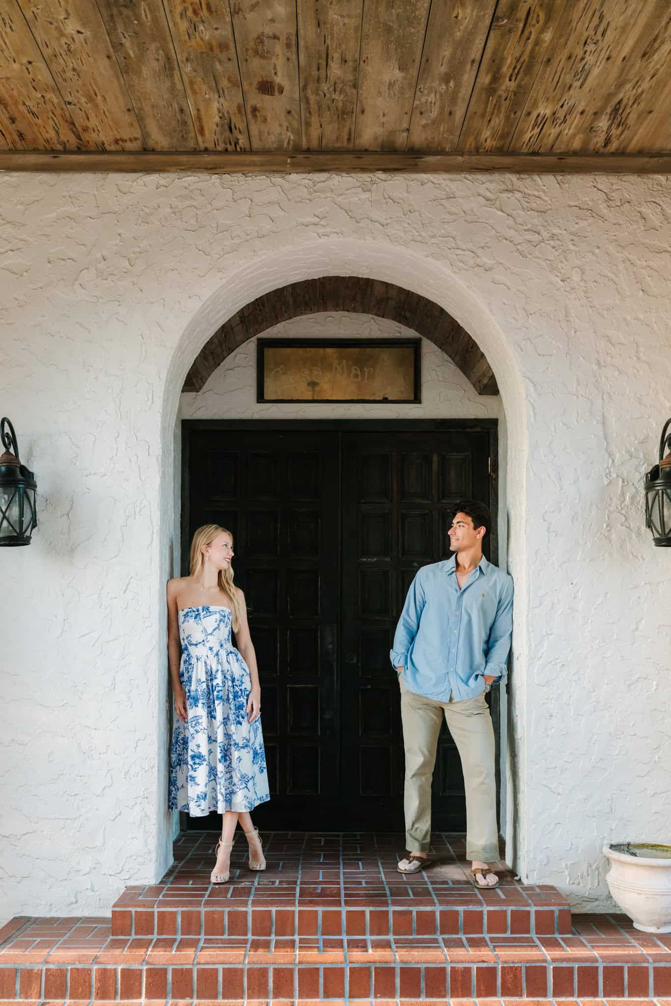 Couple posing in arched doorway of casa marina in Jacksonville Beach, woman in blue floral dress, man in light blue shirt and khakis.
