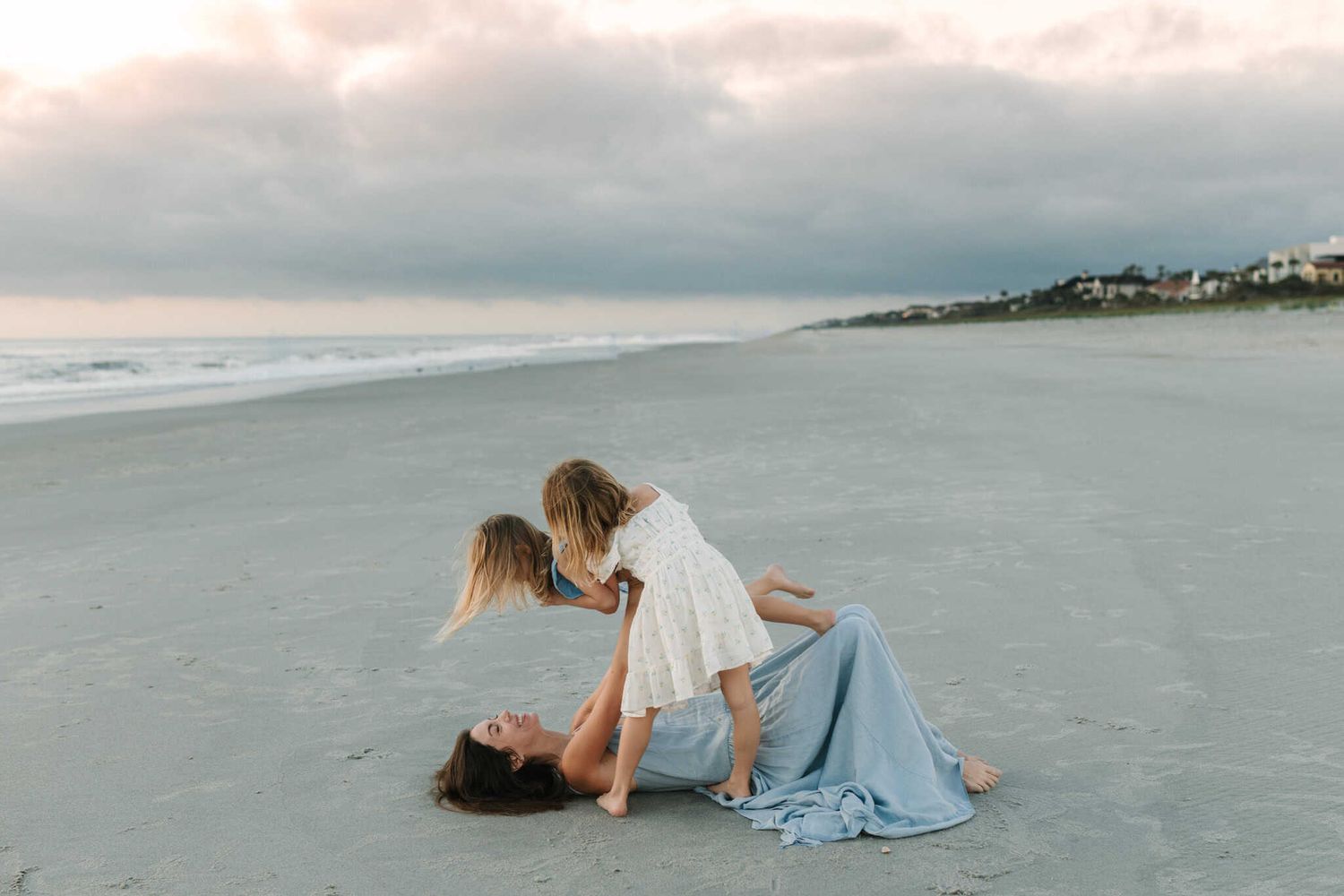 mom playing airplane with her daughters on the beach at sunrise