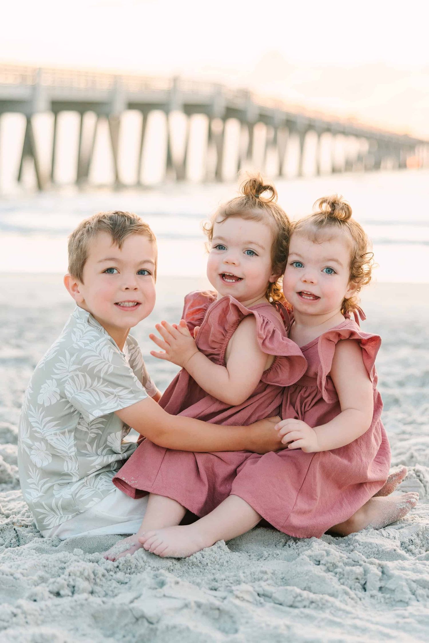 twin girls sitting on the beach with their brother at the Jacksonville Beach pier