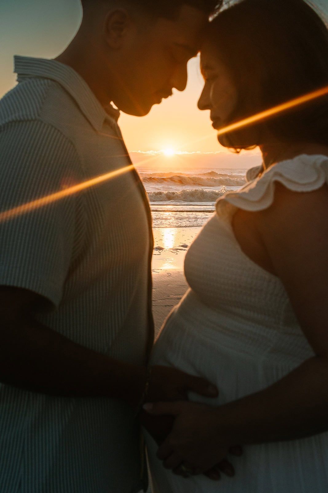 sunrise peeking through a silhouette of pregnant couple