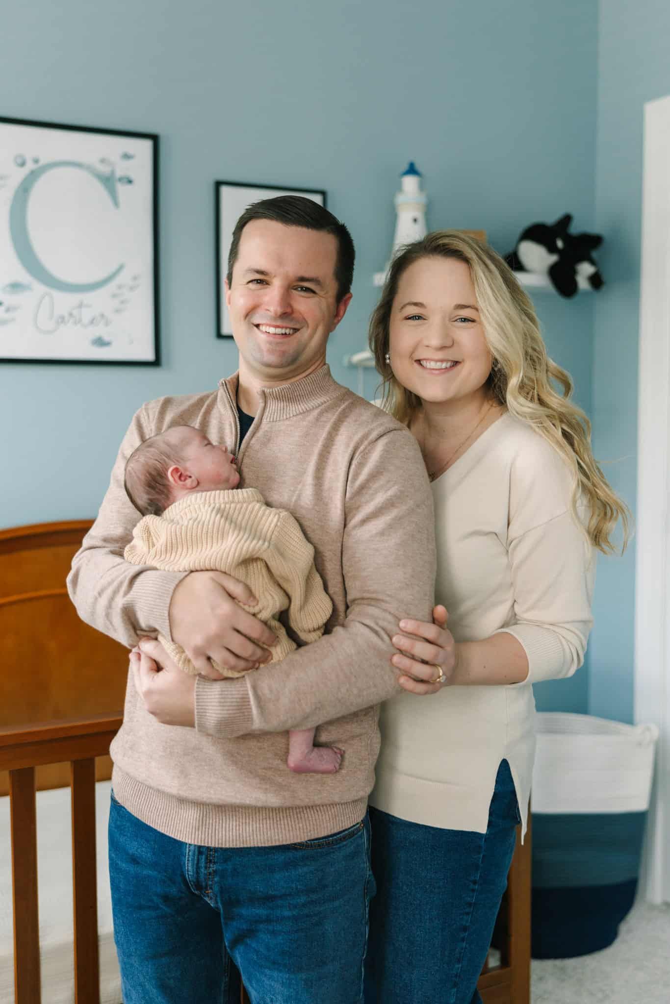 mom and dad holding newborn baby. they are wearing neutral sweaters and jeans and in the nursery in Jacksonville fl