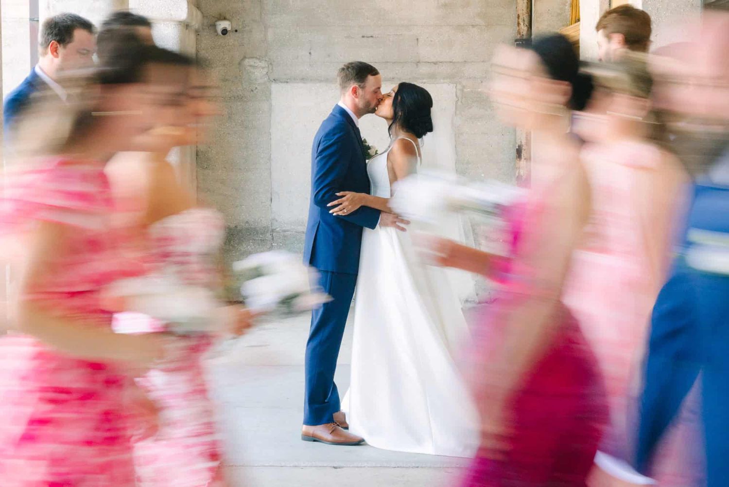 bride and groom kissing while bridal party walks by in a motion blur
