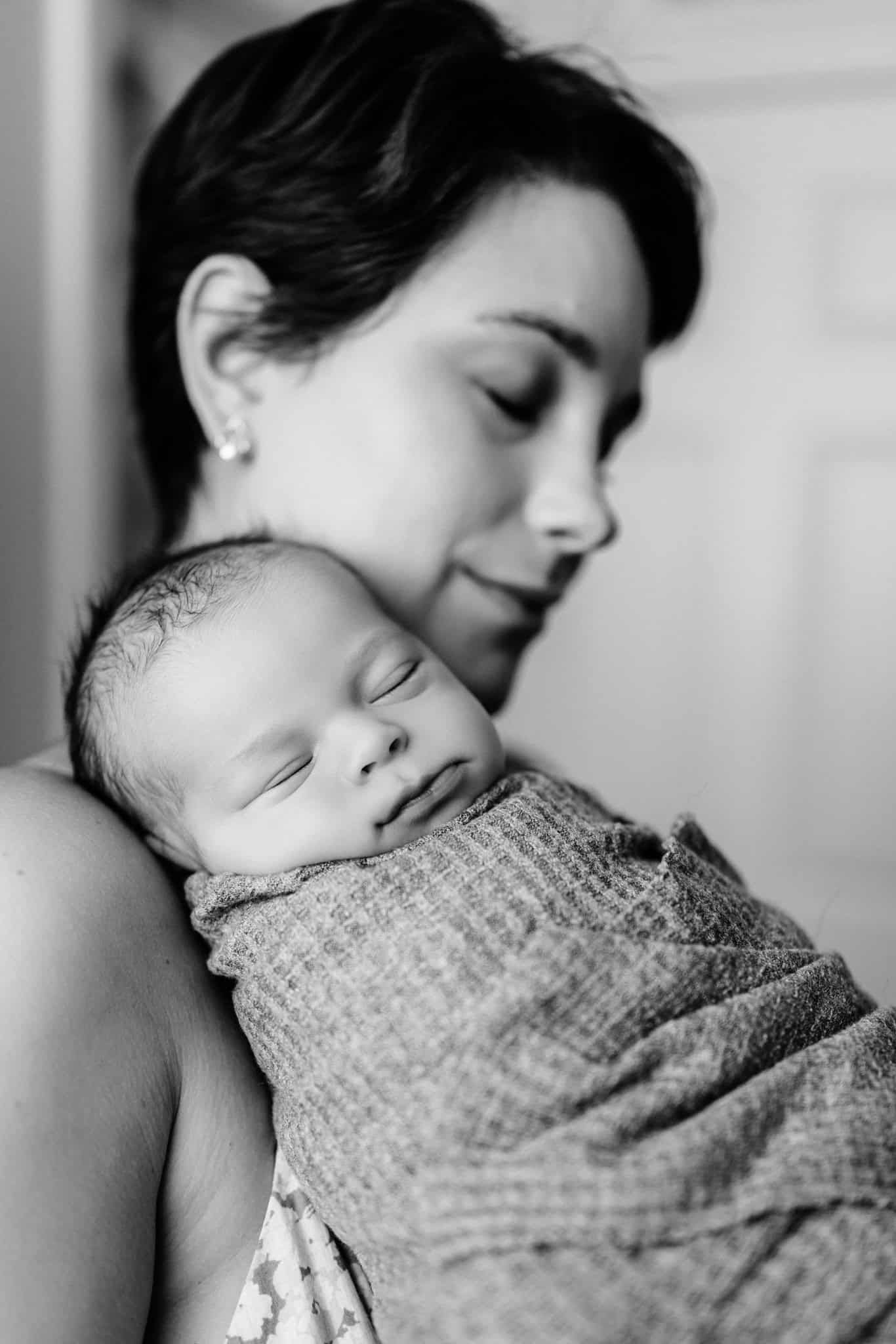 newborn baby boy swaddled snuggling on mom in black and white