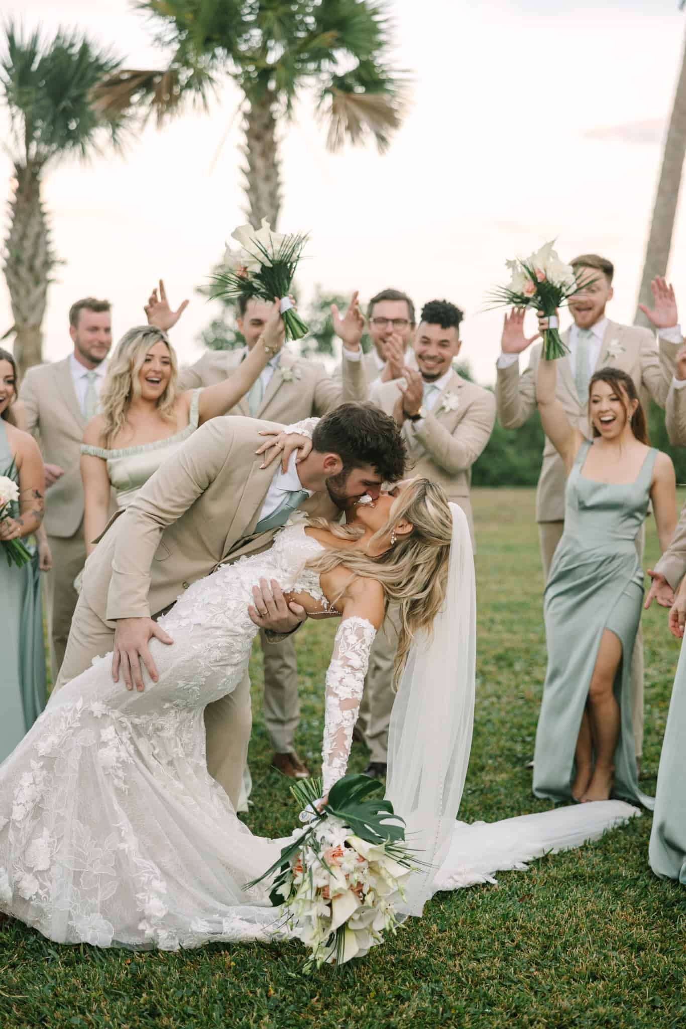 groom dipping bride for a kiss while bridal party cheers them on