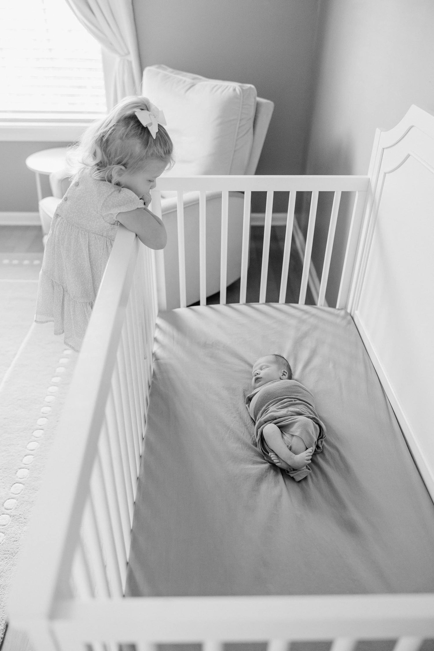 black and white of older sister looking down into the crib at her newborn brother