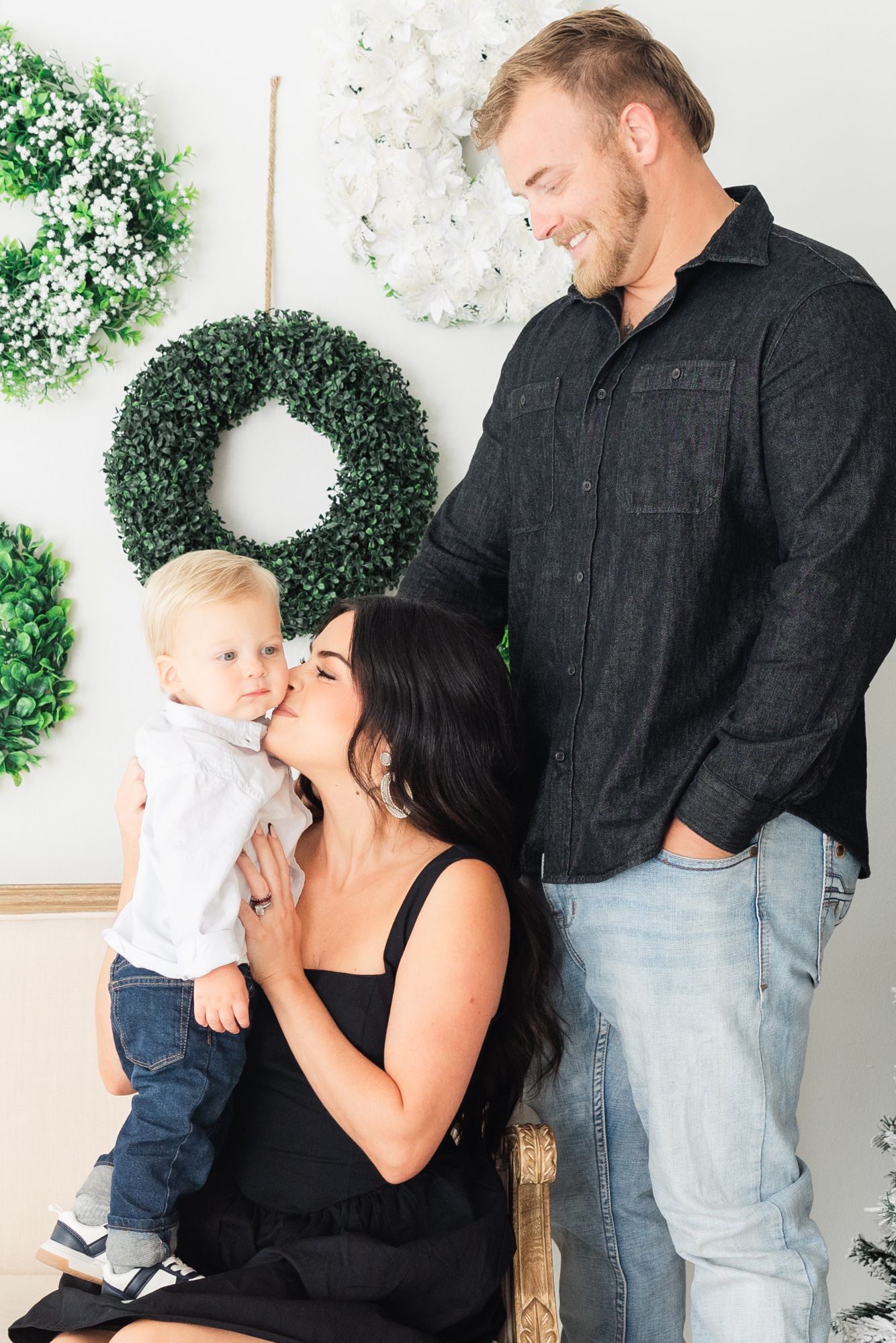 mom kissing son wearing black dress and Christmas wreaths behind them