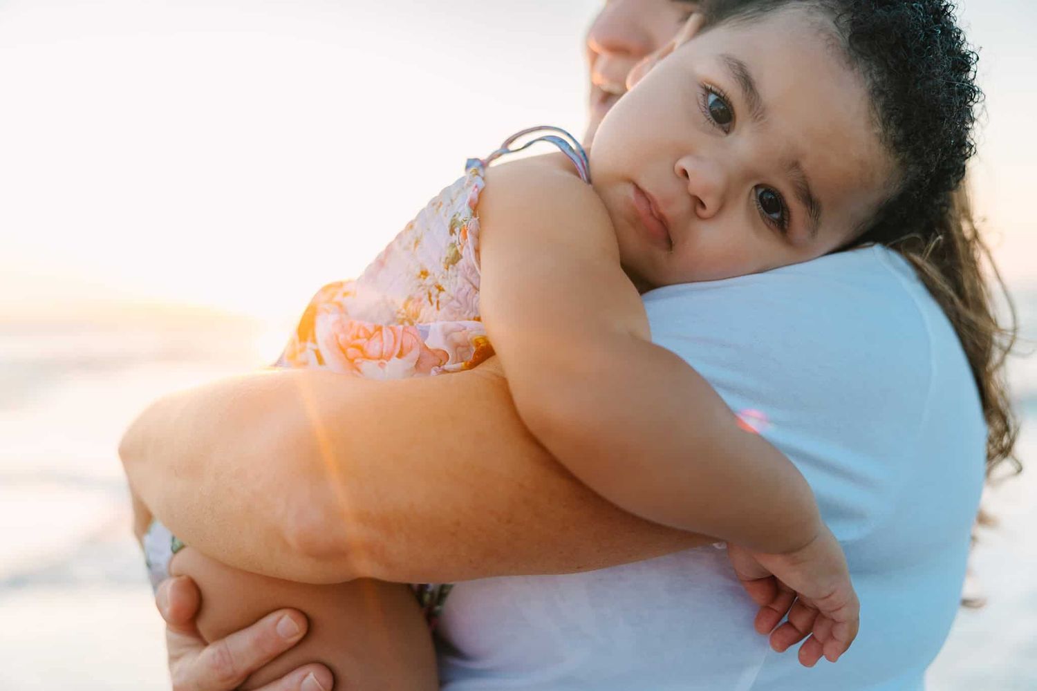 toddler girl snuggling with grandma with beach sunrise peeking over