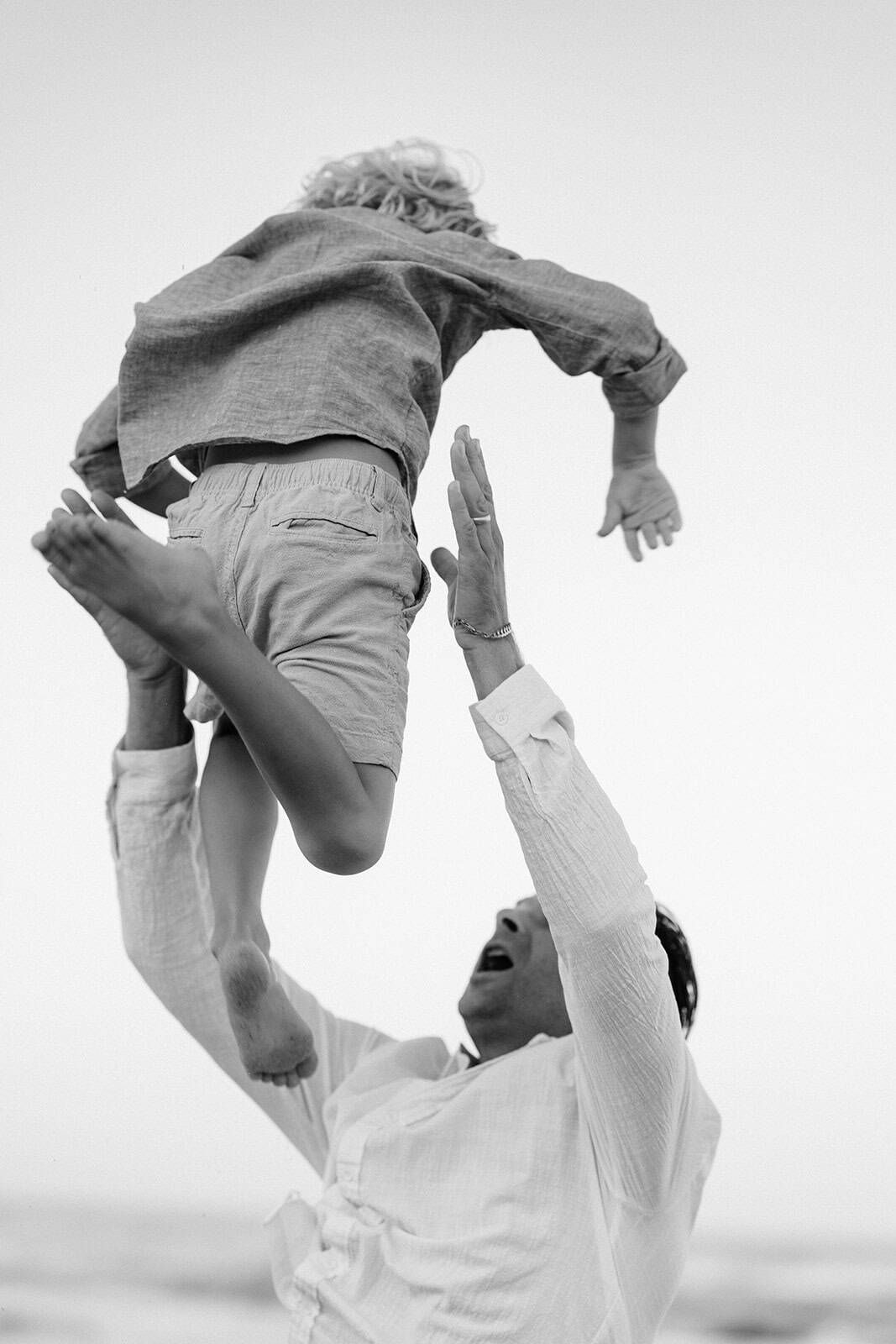 black and white image of dad throwing son up into the air