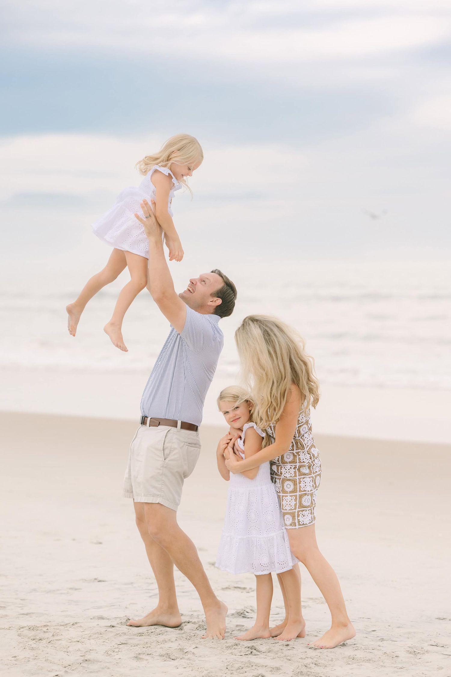 dad tossing daughter in the air while mom and daughter snuggle