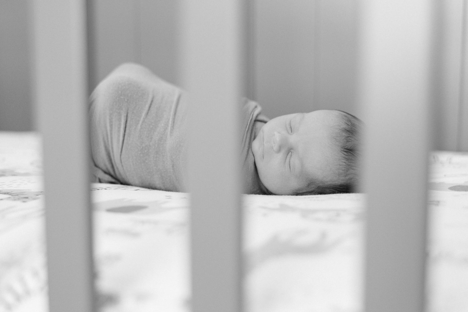 black and white newborn baby in crib peeking through the crib