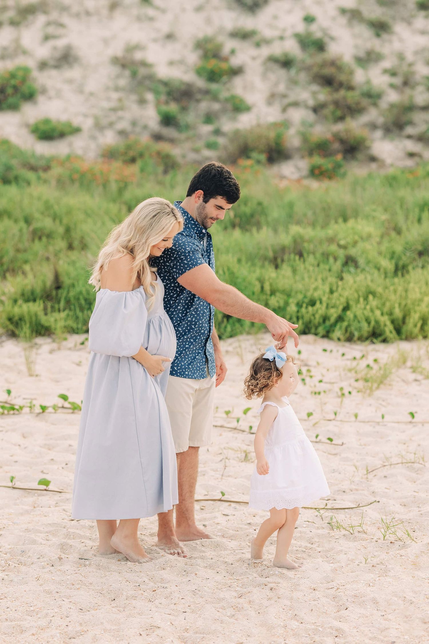 pregnant mama hugging her husband who is twirling their older daughter on ponte vedra beach in the sand