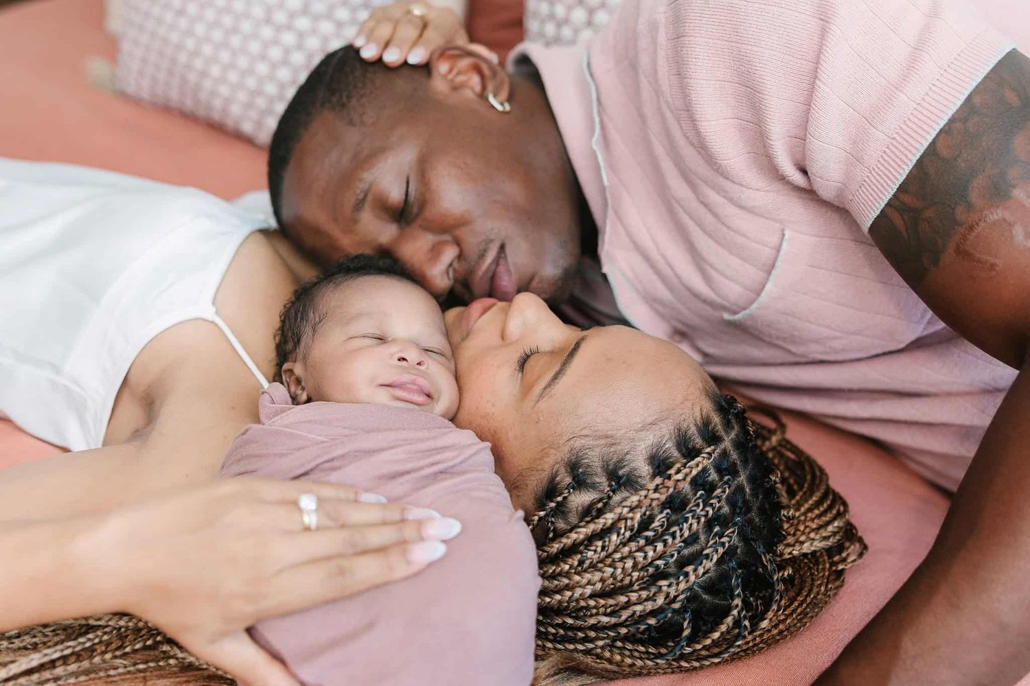 from above and the side, newborn baby swaddled laying on moms chest with dad snuggling from the other side of mom