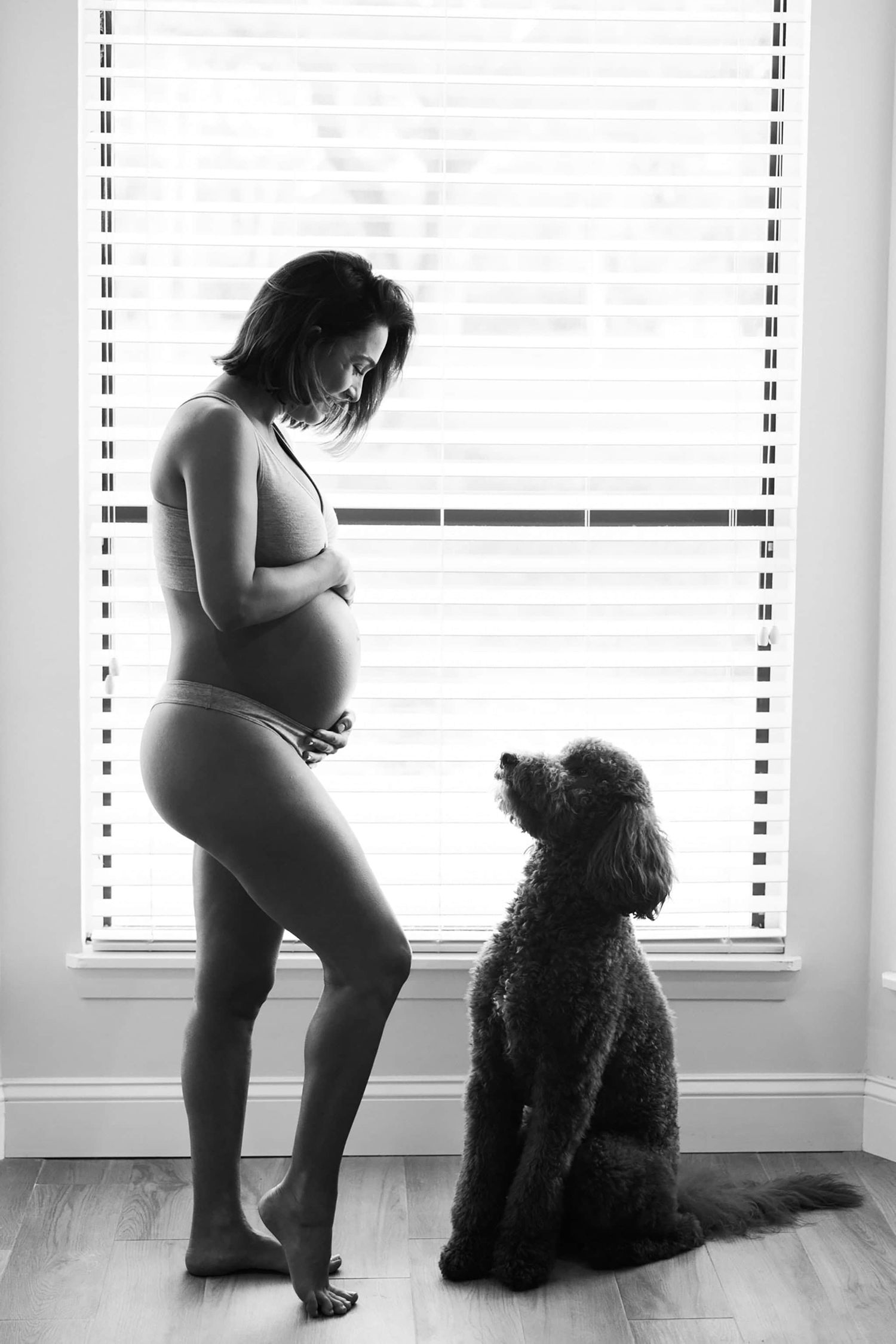 black and white of woman holding pregnant belly and her and the dog looking at each other