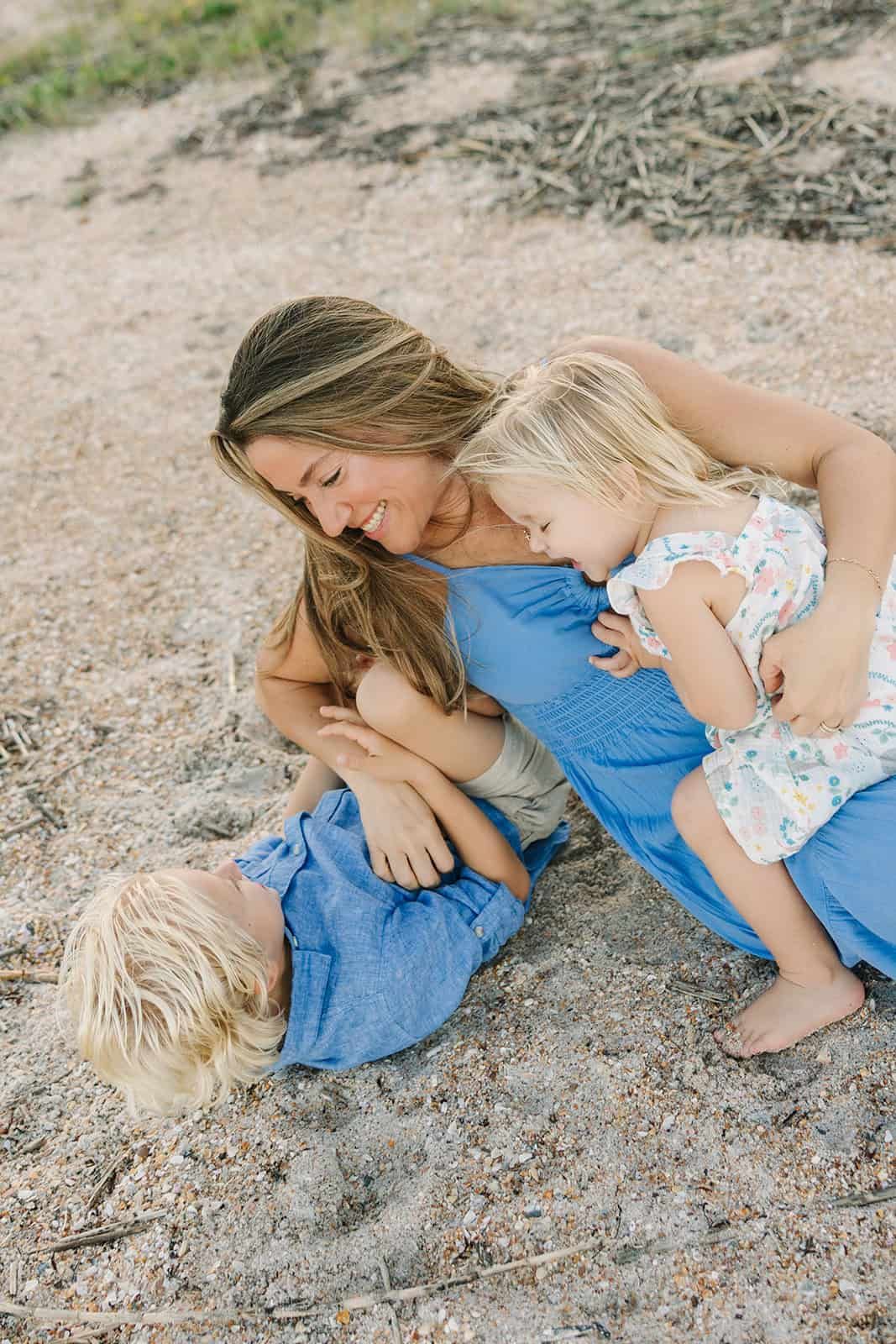 mom playing with son in the sand at Jacksonville Beach and daughter snuggling on mom