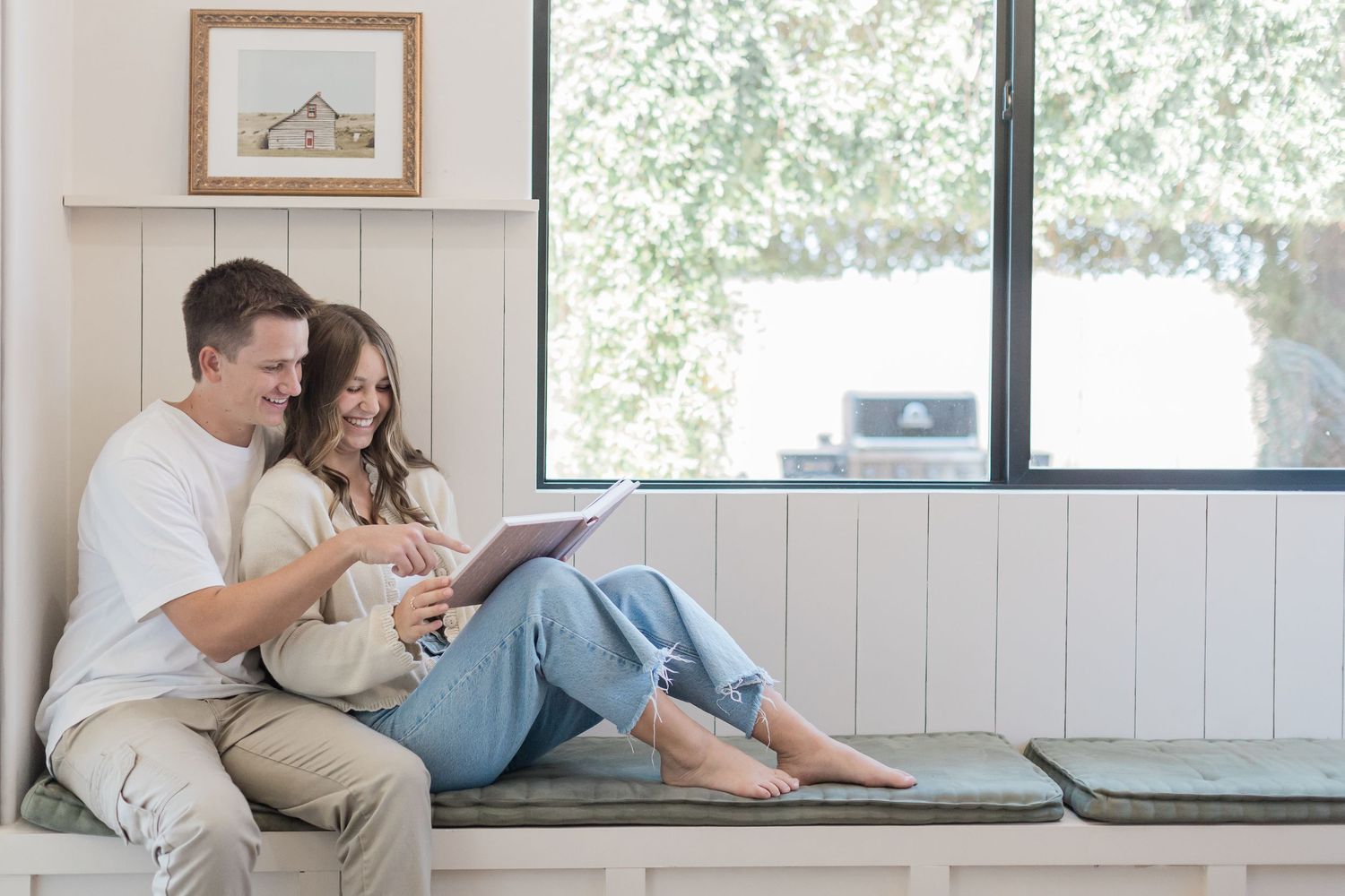 Happy couple sitting on a window bench seat, smiling and looking at an heirloom album together in a bright Saint Augustine home.