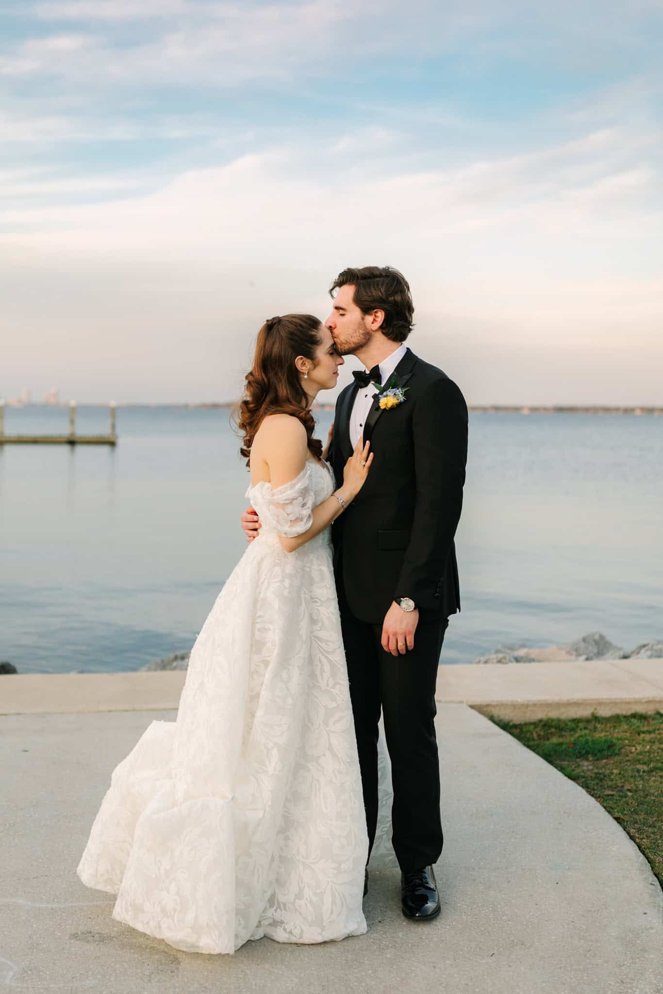 full body of groom kissing bride on her forehead