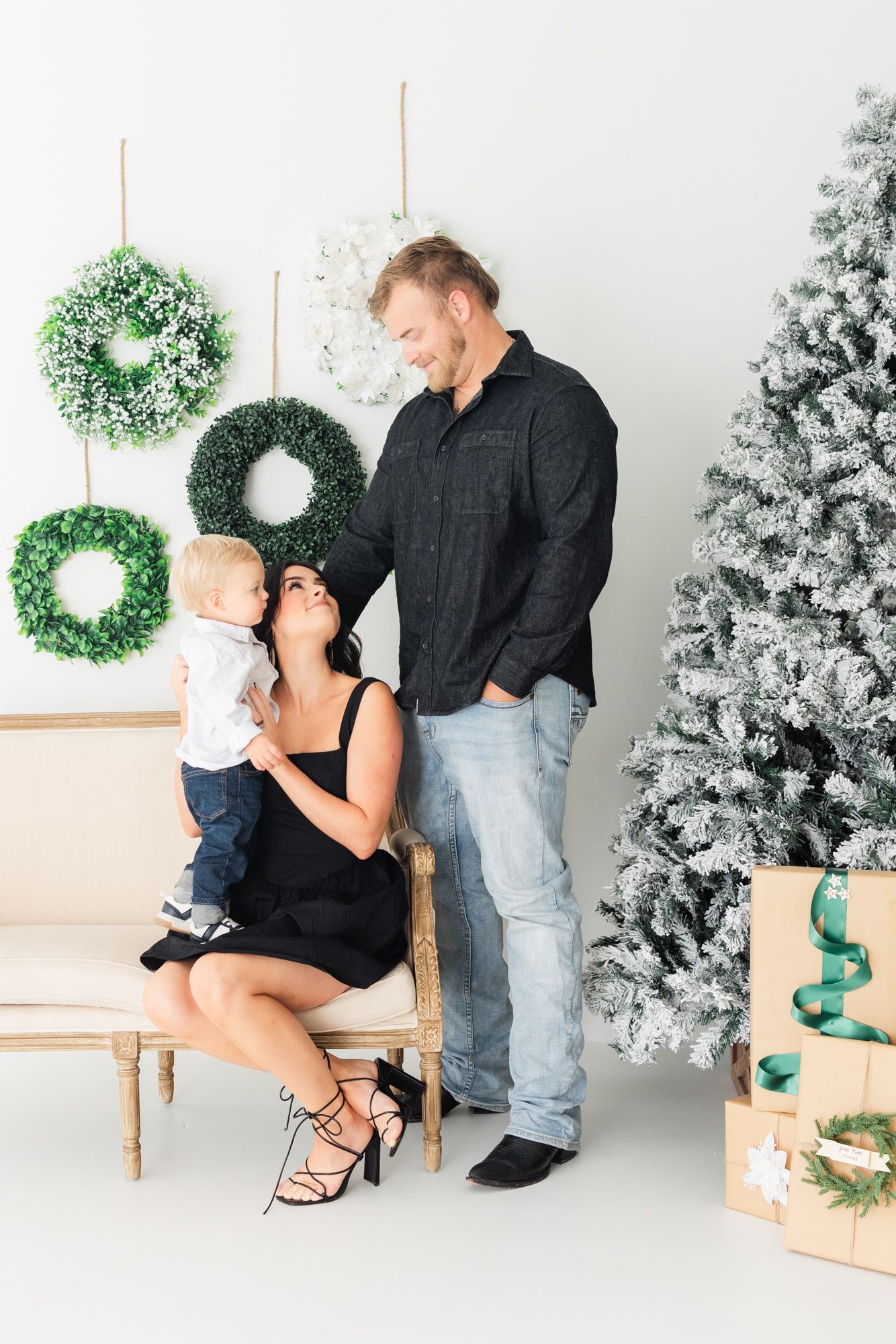 family of three looking at each other at Christmas mini session in Jacksonville fl with wreaths and a Christmas tree
