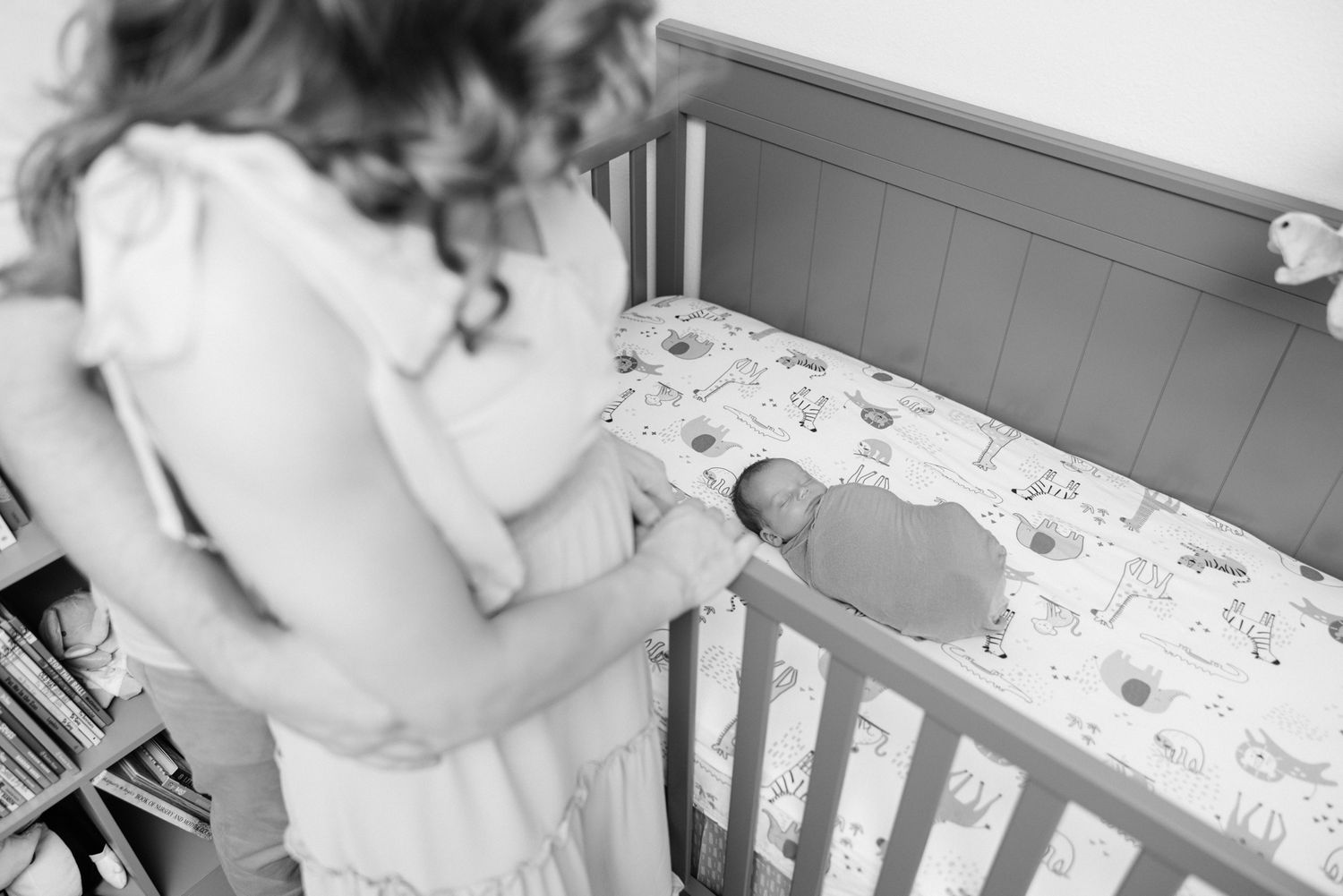 black and white of parents looking at newborn baby so small in his crib