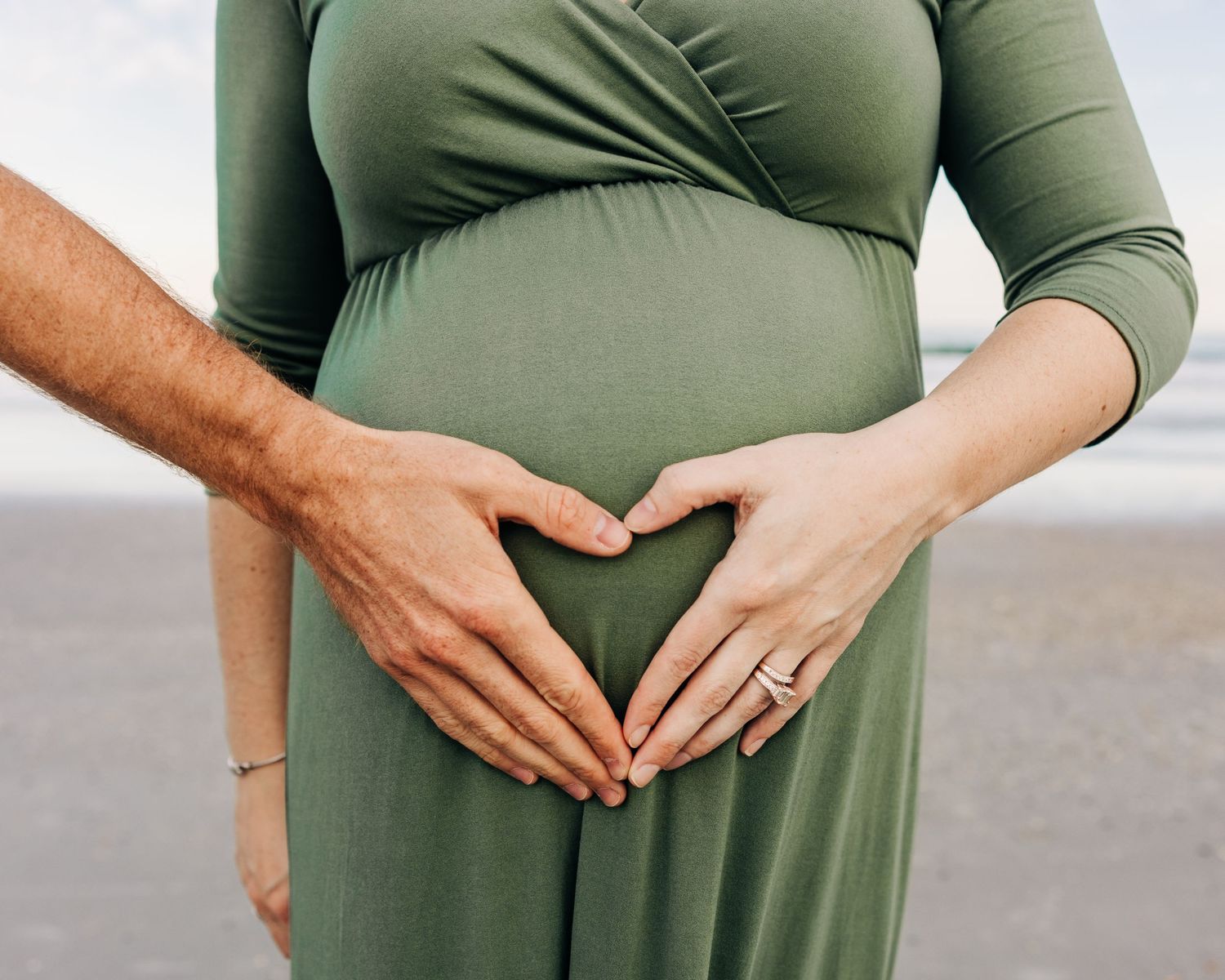 pregnant belly on jacksonville beach with parents hands making a heart