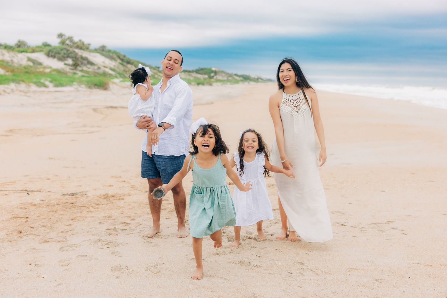 family of 5 in jacksonville beach fl with older daughters running toward the camera and parents laughing
