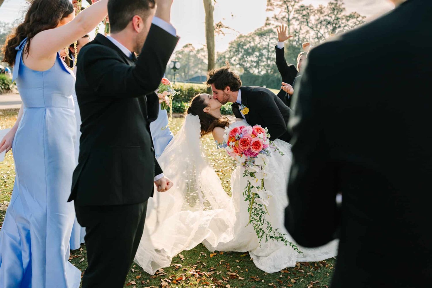groom kissing bride while bridal party cheers them on