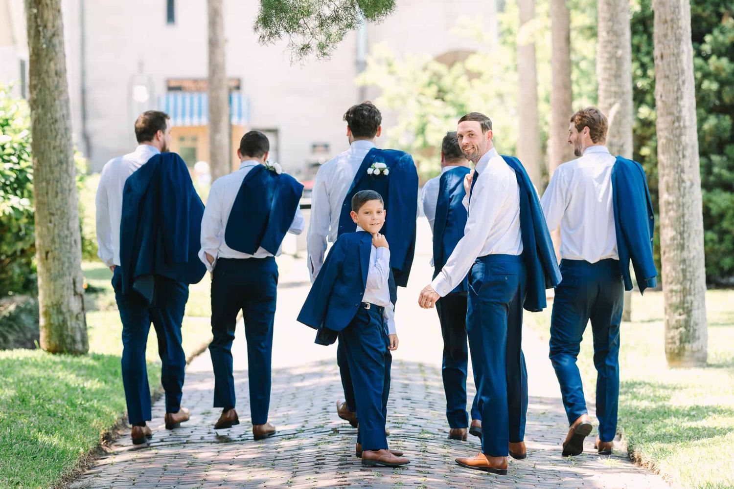 groom and his groomsmen walking away while him and his son look back at the camera