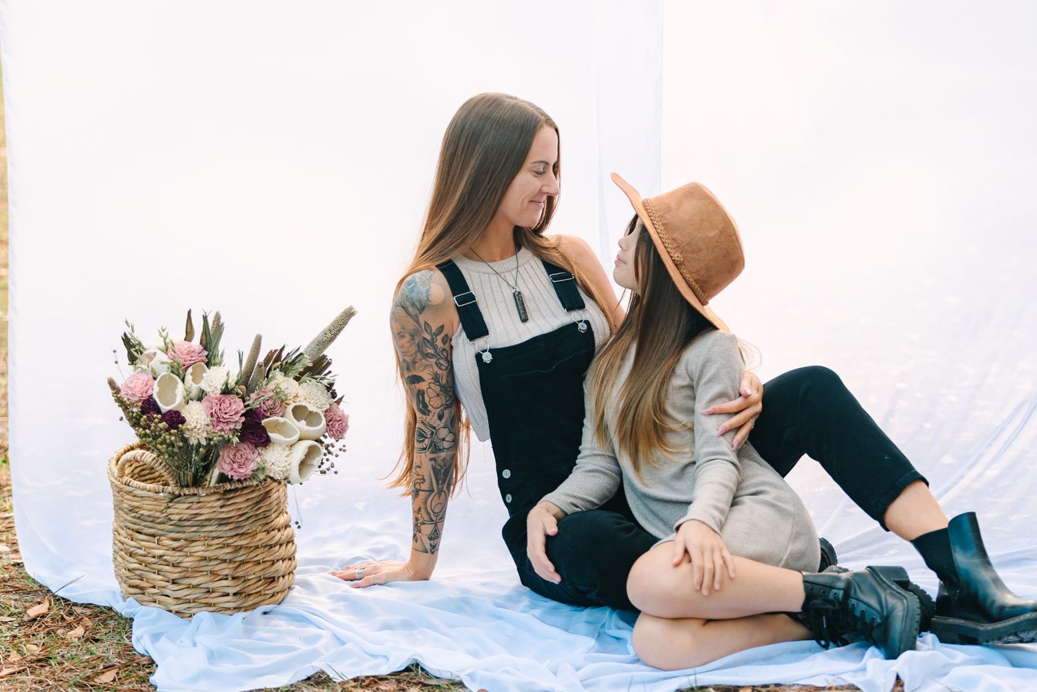 mom and daughter sitting smiling at each other with a hanging sheet and basket of pretty flowers