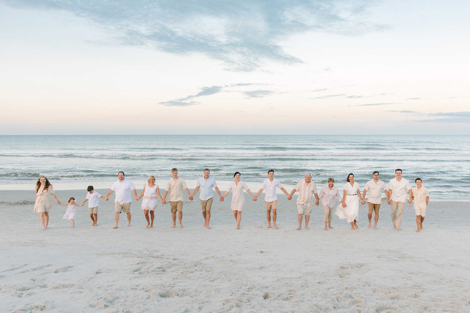 large extended family holding hands looking at the camera at the beach