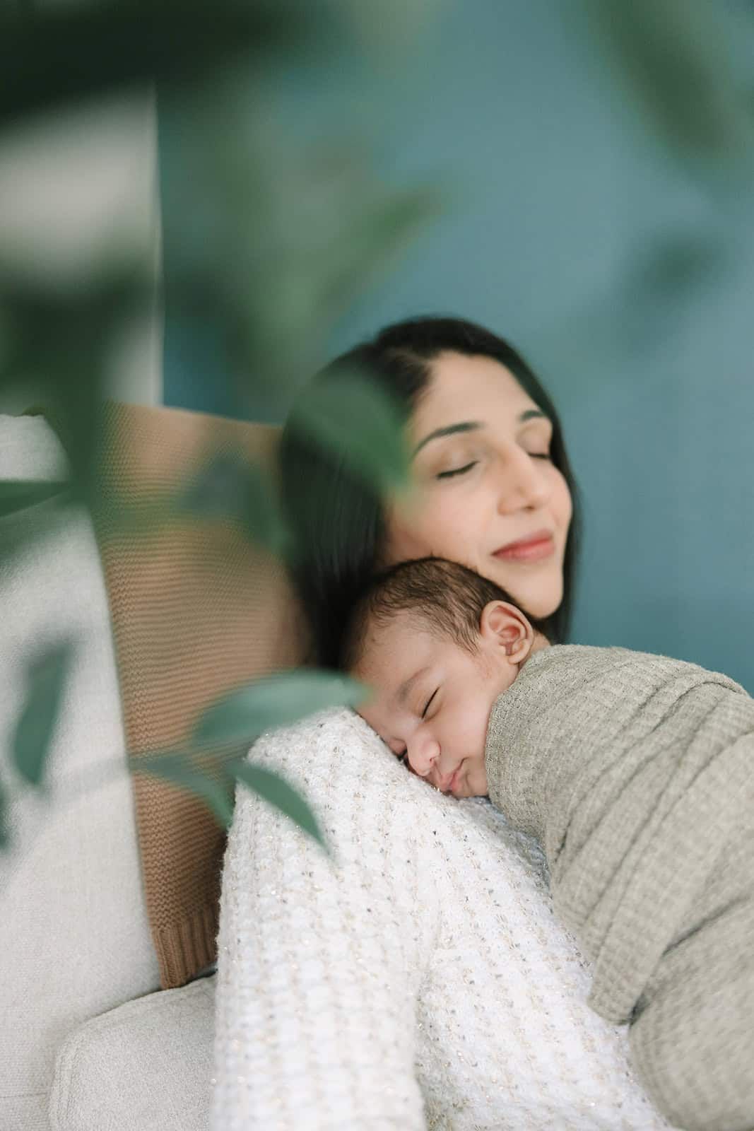 mom sitting in glider snuggling newborn baby peeking through the tree in baby's nursery