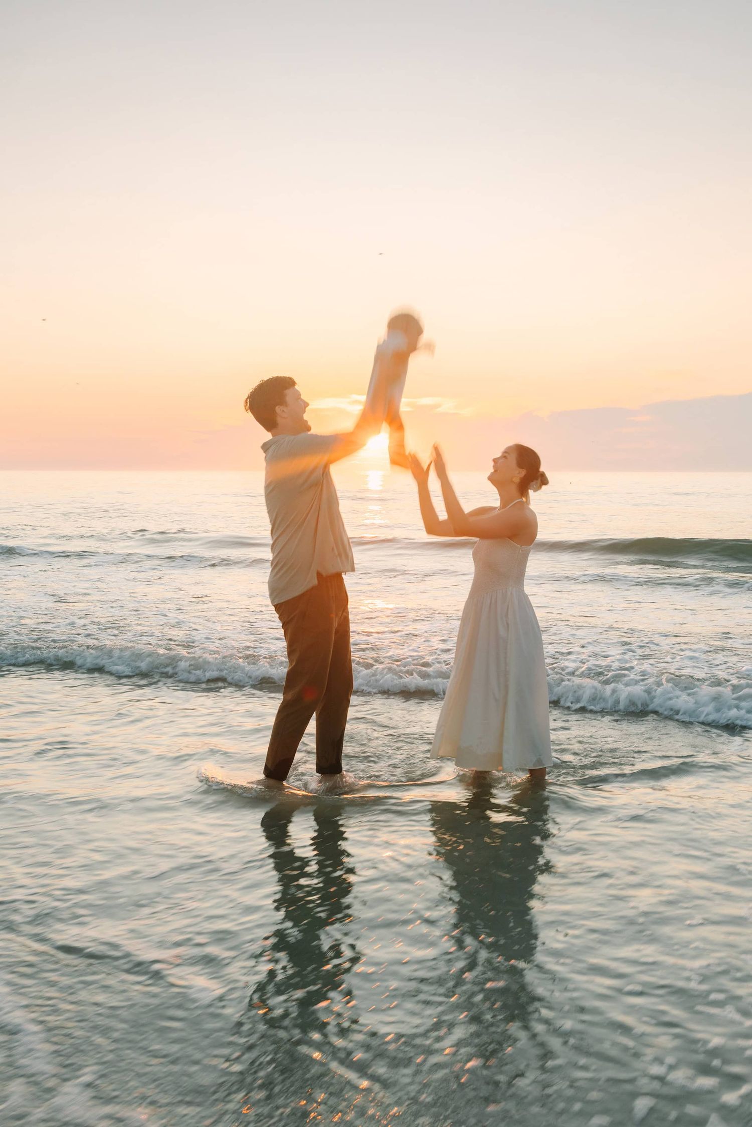 sunrise at Jacksonville Beach fl with dad tossing young son in the air to mom with sun poking out from behind them