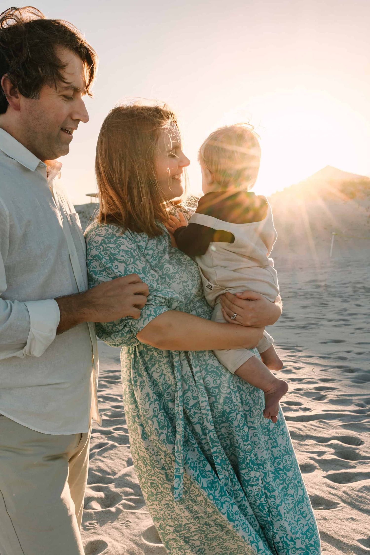 mom holding sun with sun rays peeking over his shoulder and dad holding mom