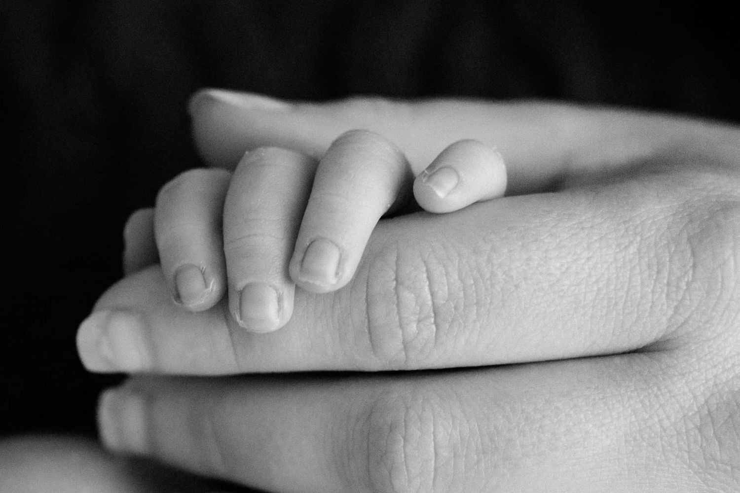newborn baby fingers holding onto moms hand in black and white