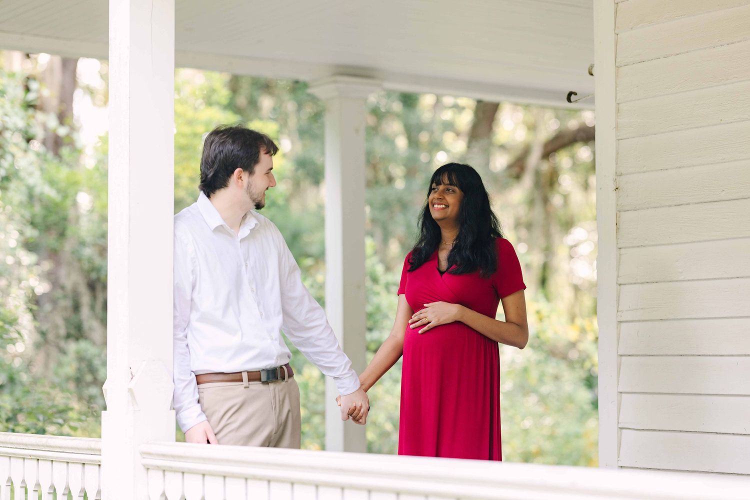 pregnant couple holding hands in cute white house porch
