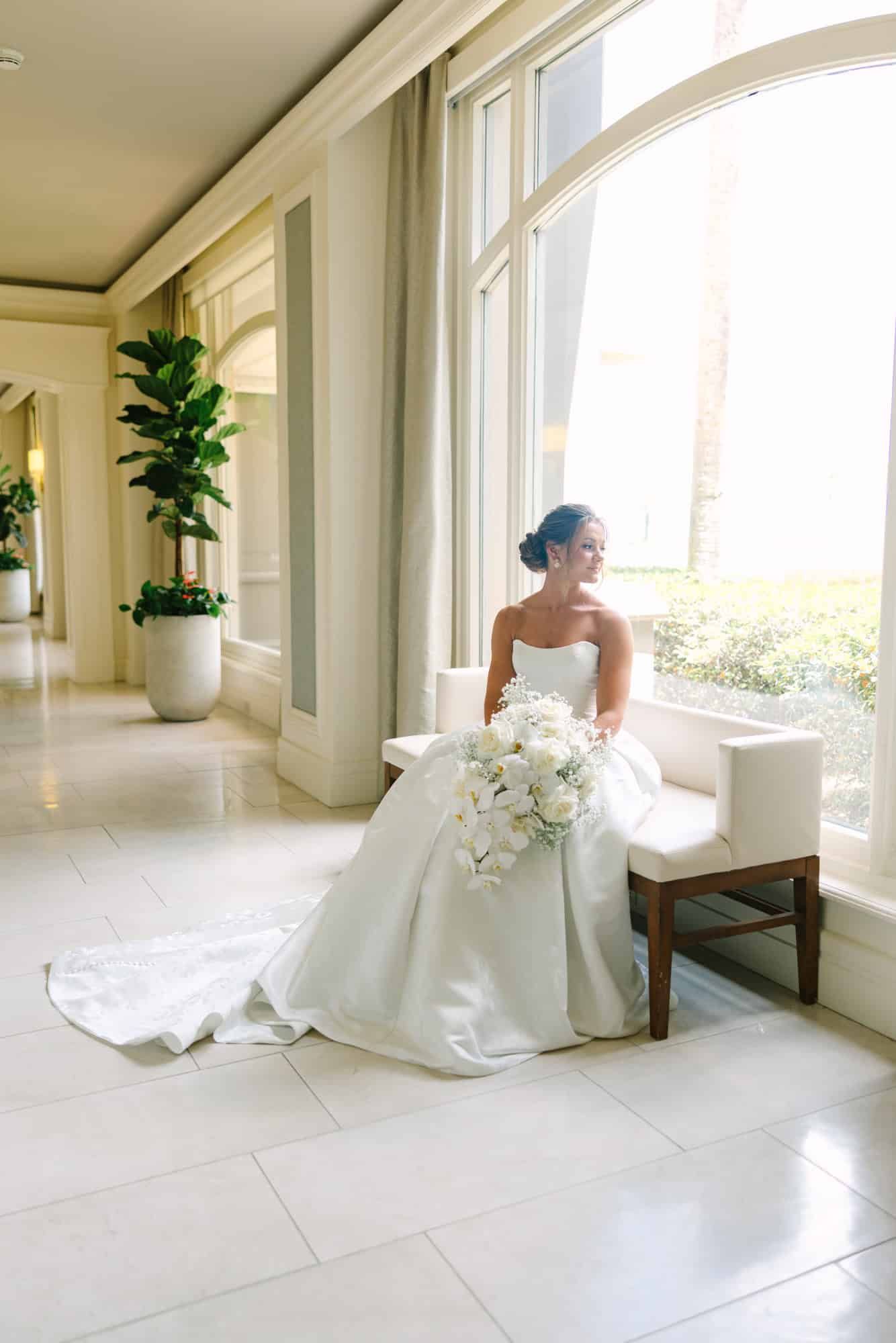bride sitting in a white hallway looking out the window