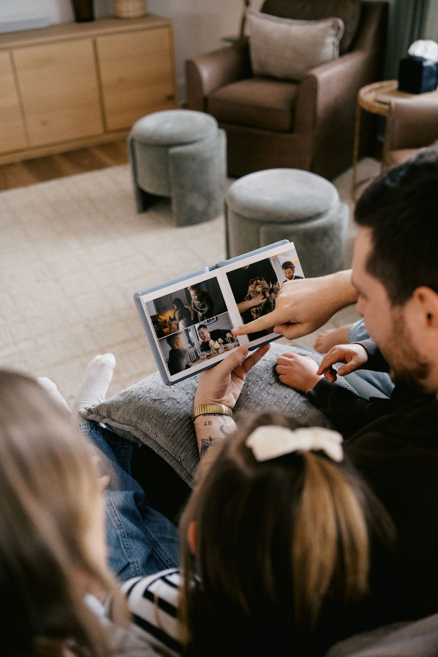 Family sitting together on a couch looking at a photo album in a cozy living room.