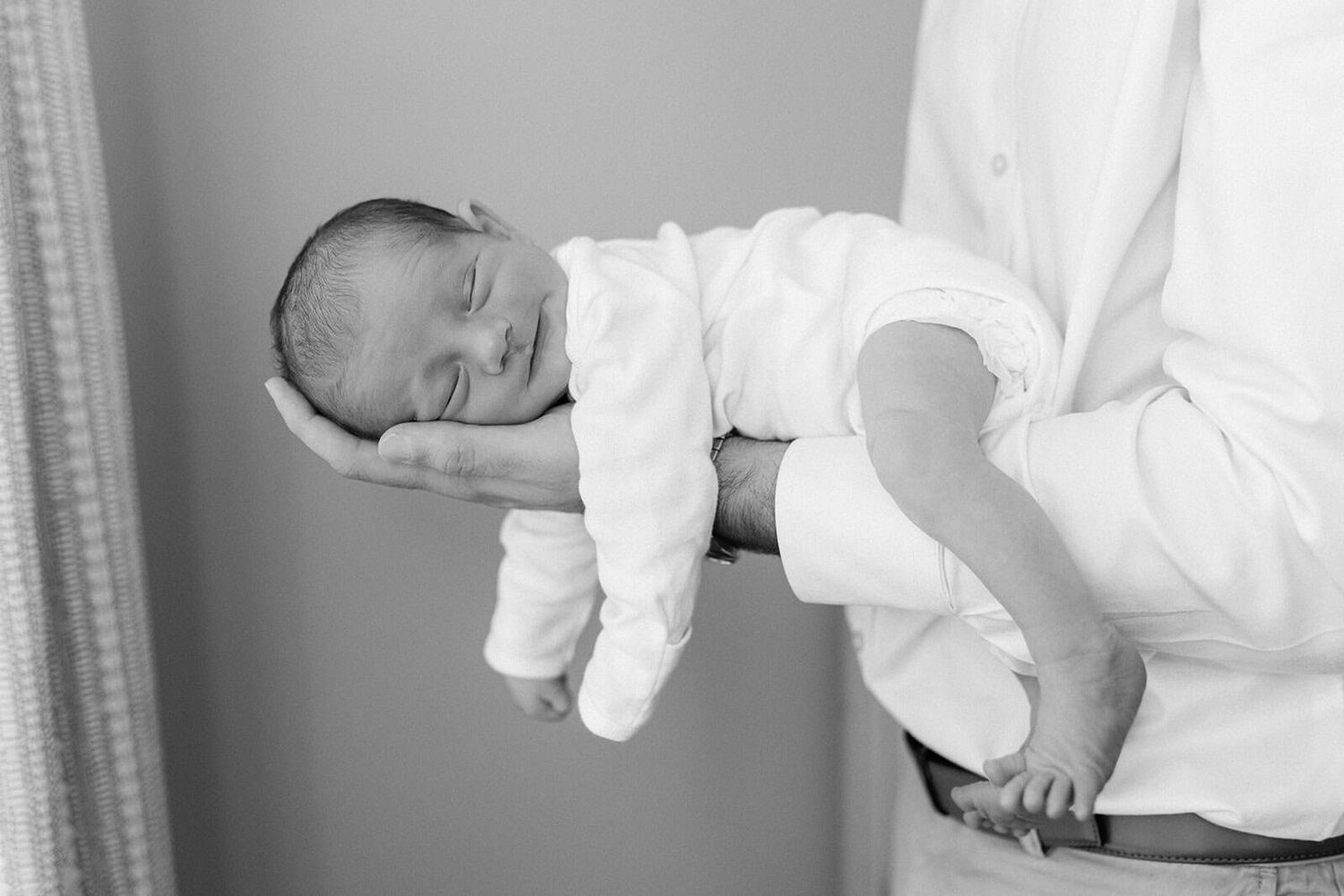 black and white photo of newborn baby boy laying on dads arm so small with his head in dad's hand