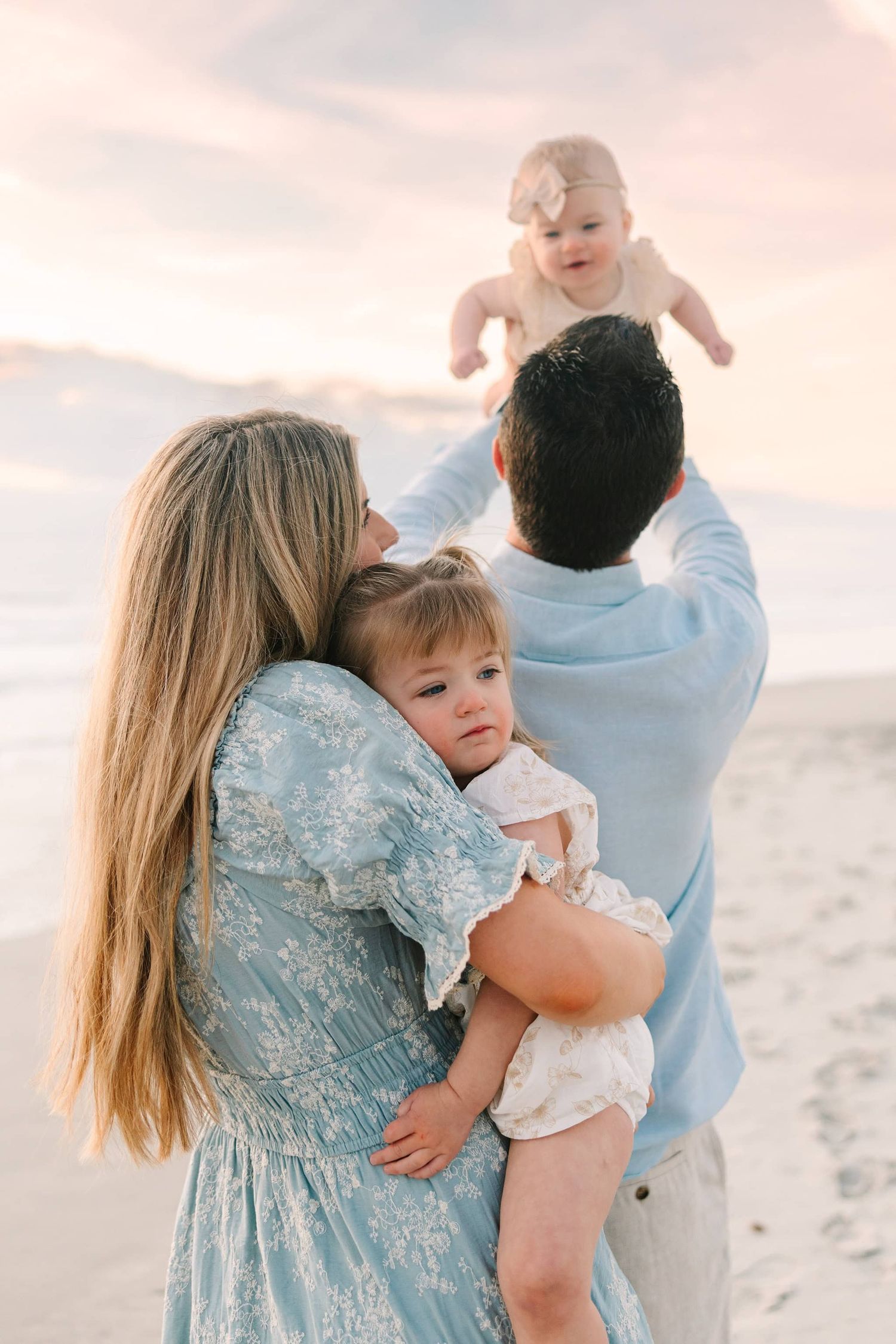 dad throwing youngest in the air behind mom snuggling with older daughter