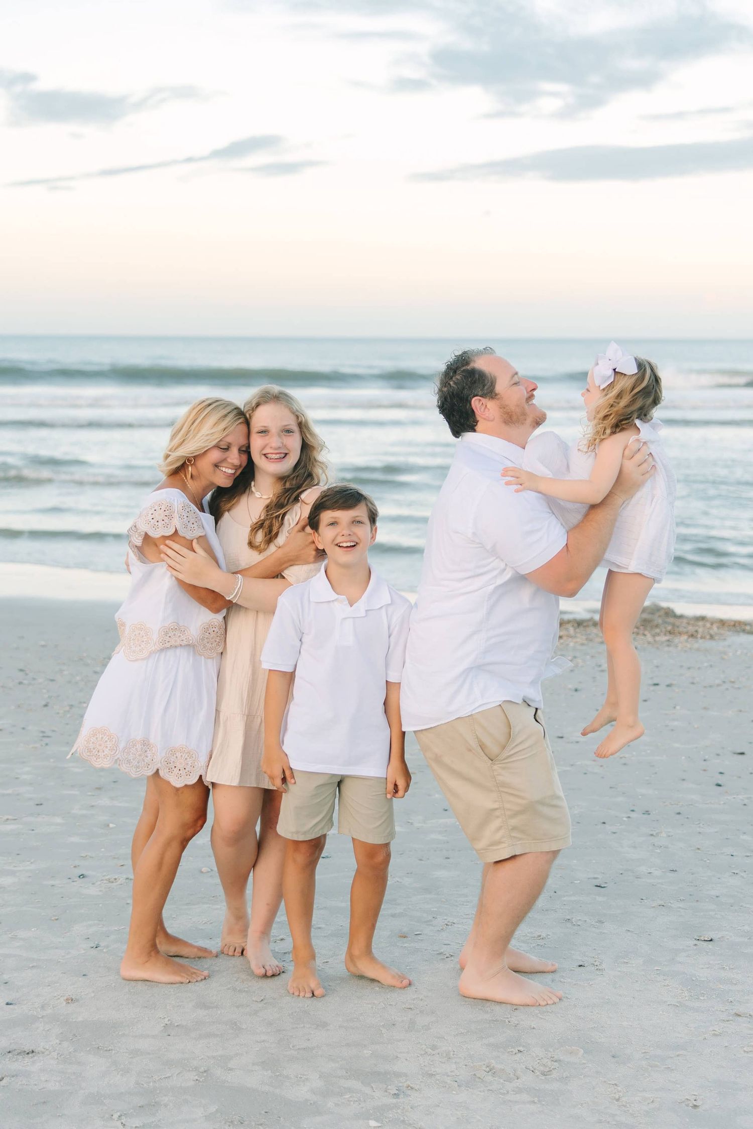 mom snuggling with daughter while dad throws youngest into the air at the beach