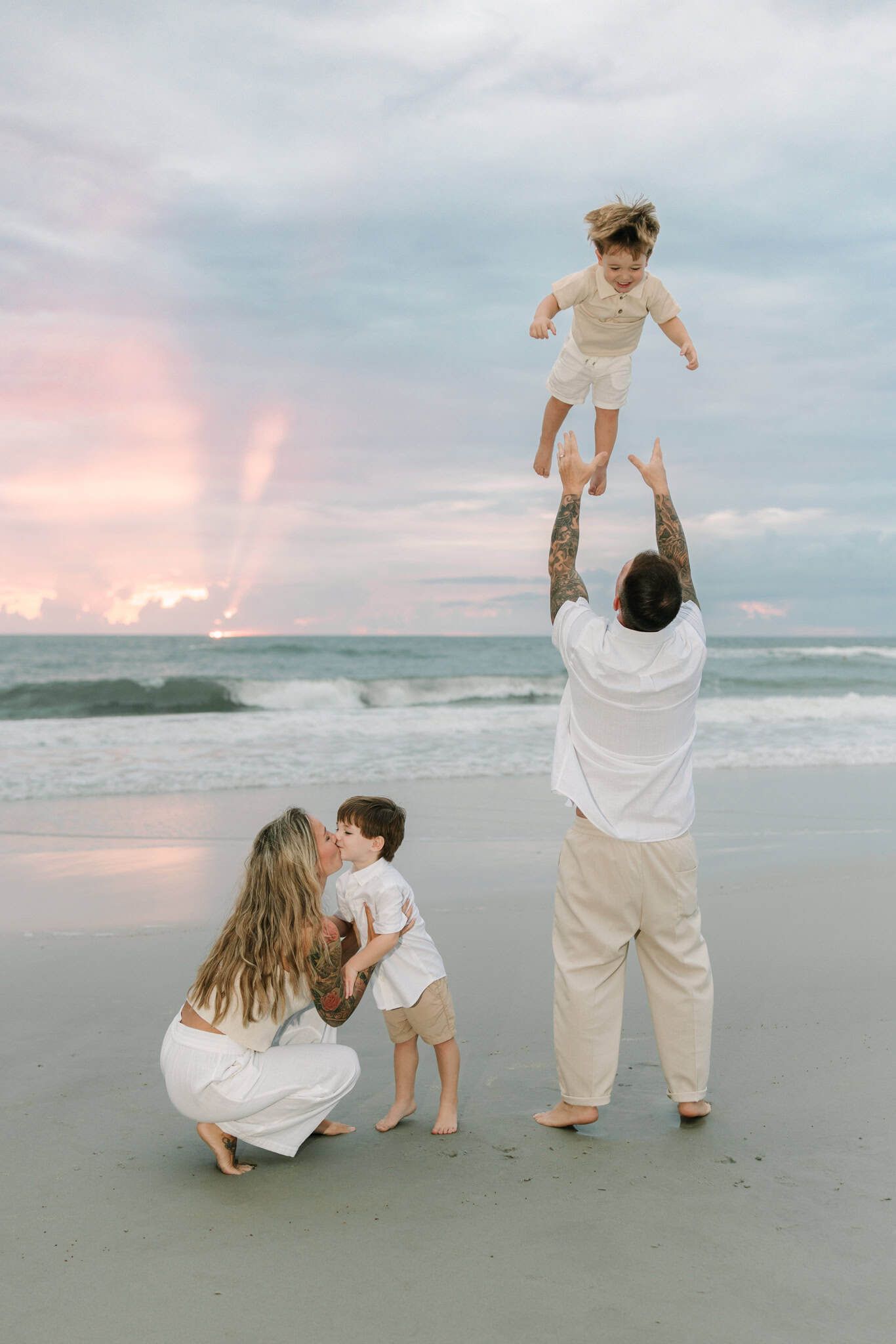 Family playing on beach at Jacksonville Beach sunrise, father tossing child in air while mother crouches with toddler by ocean waves